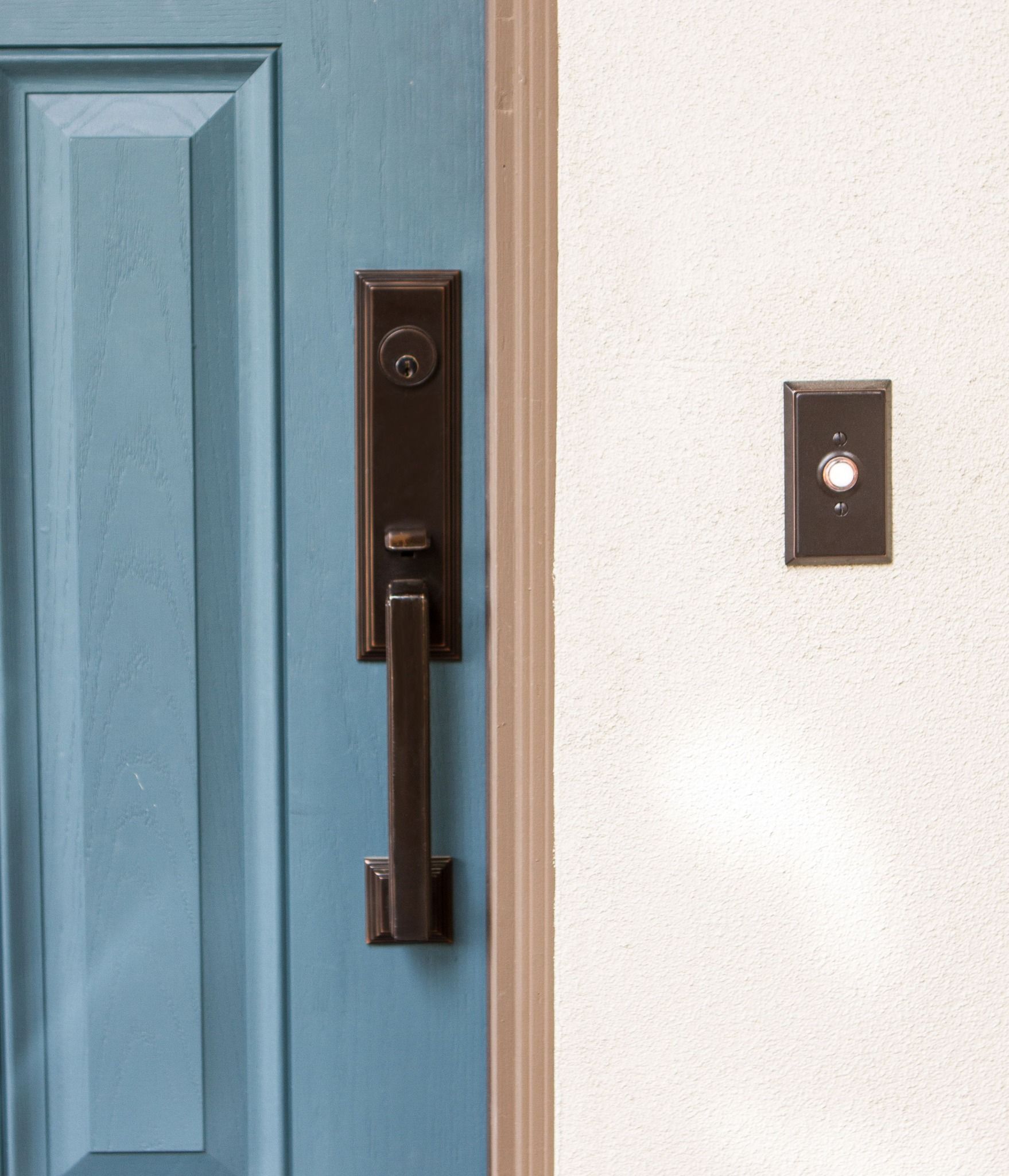 Blue door with dark bronze handle and a doorbell on a white wall.