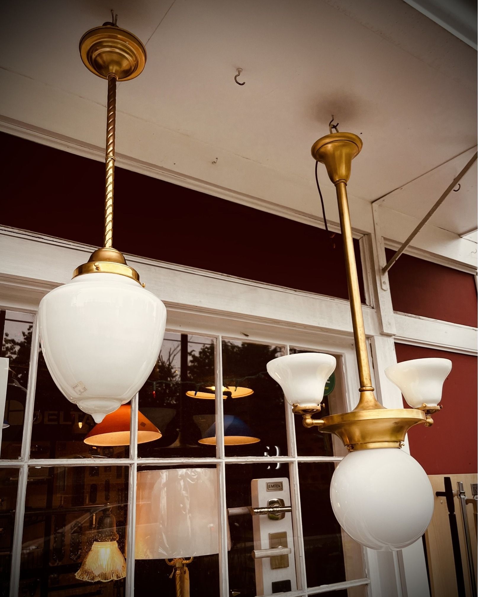 Two antique gold and white pendant lights hanging from a white ceiling, in front of a window.