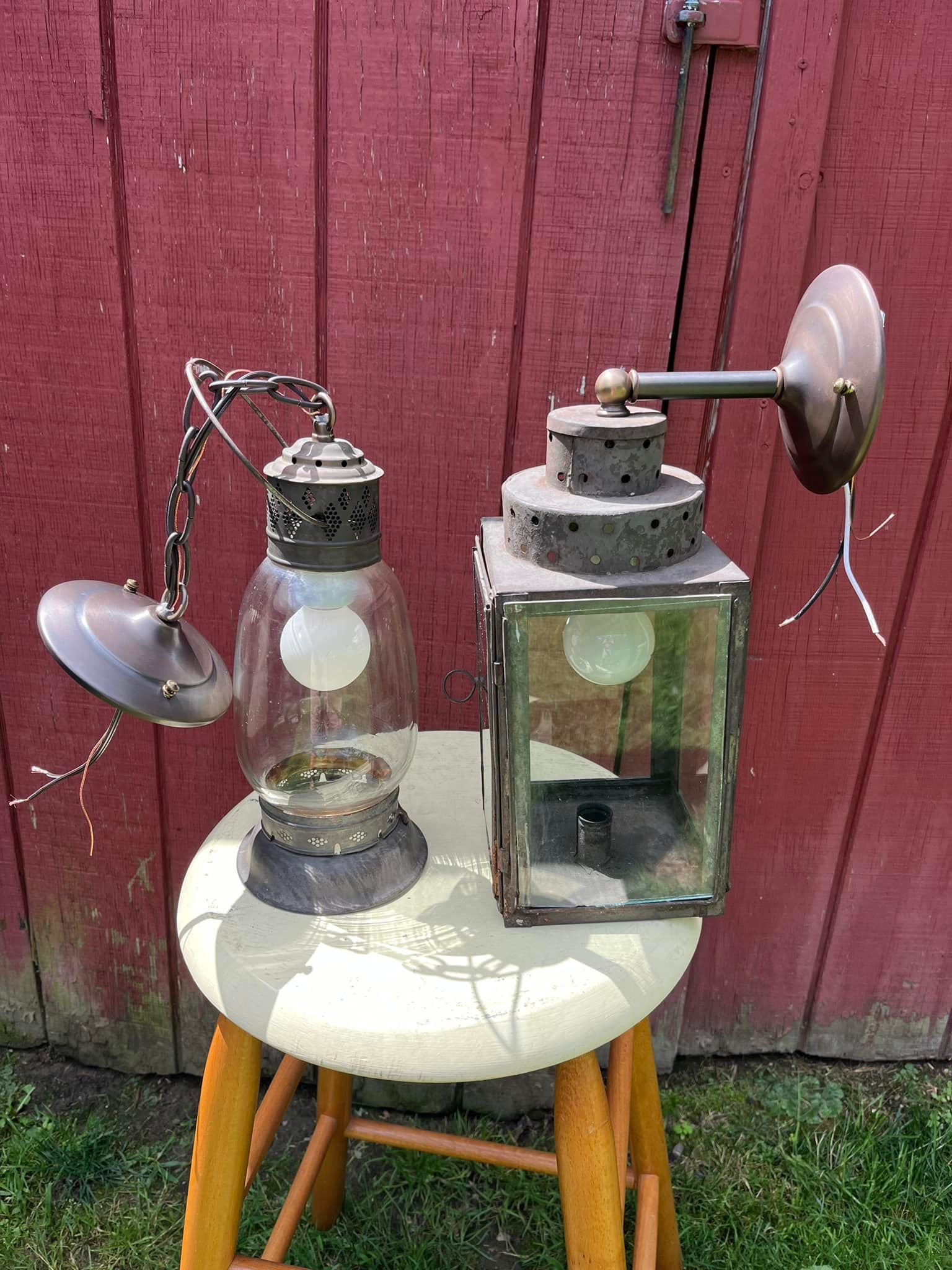 Two antique lanterns on a stool against a red wooden wall. One hangs from a chain.
