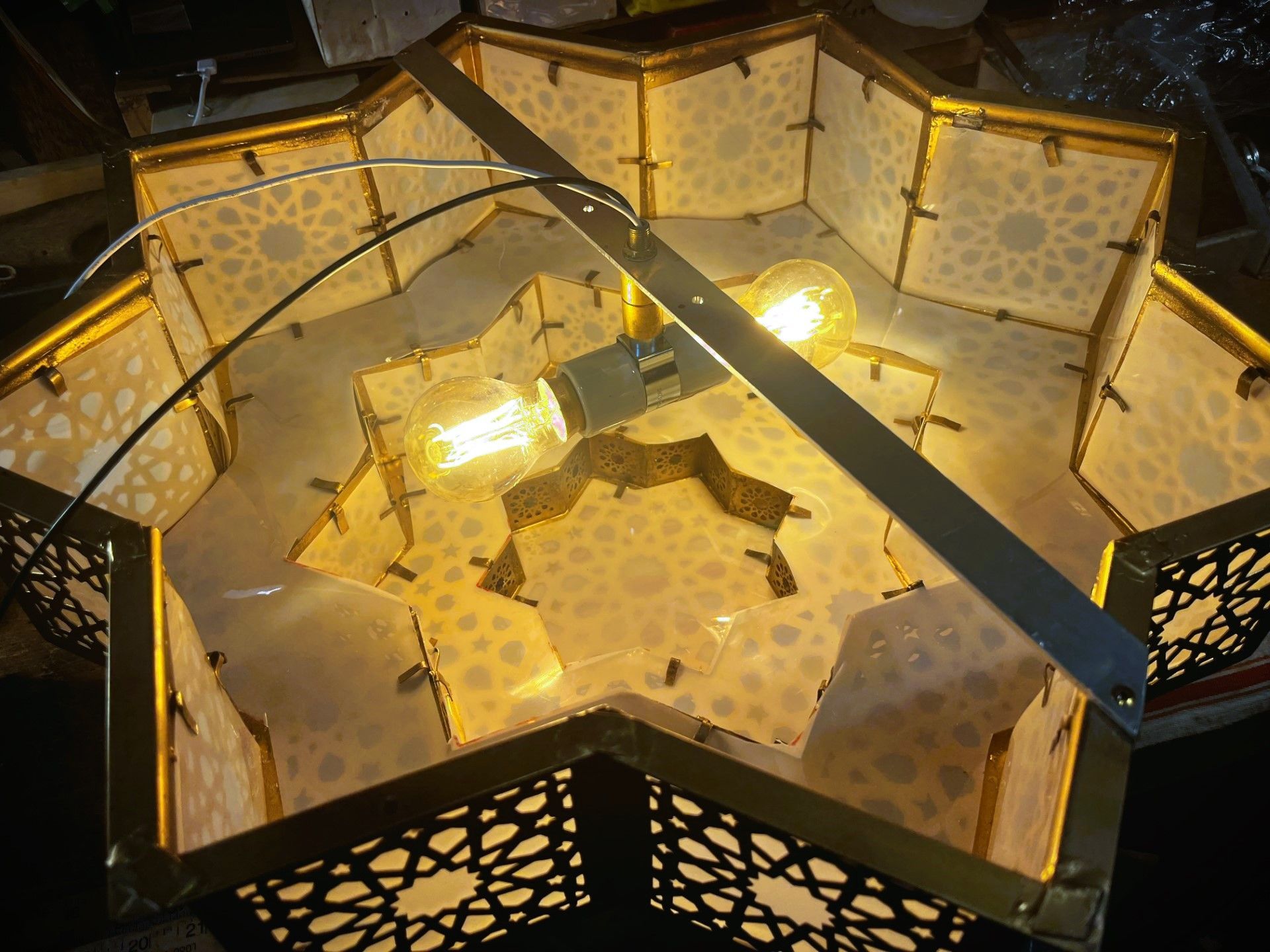 A star-shaped pendant lamp with two lit light bulbs. Brass-colored frame with patterned cutouts.