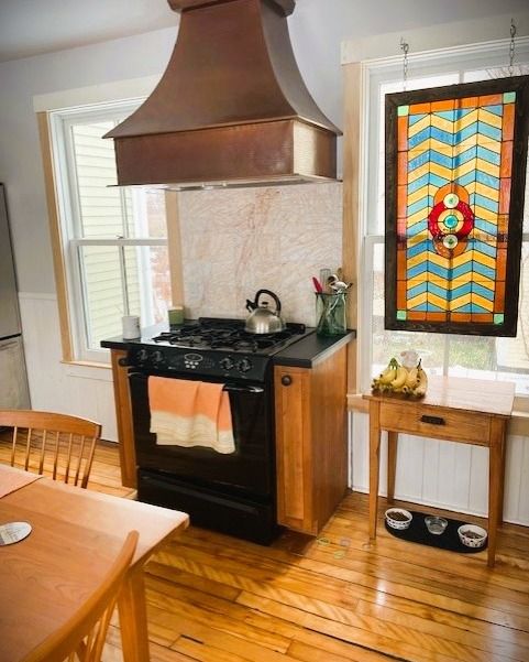 Kitchen with copper hood, black stove, stained glass window, and wood floor.