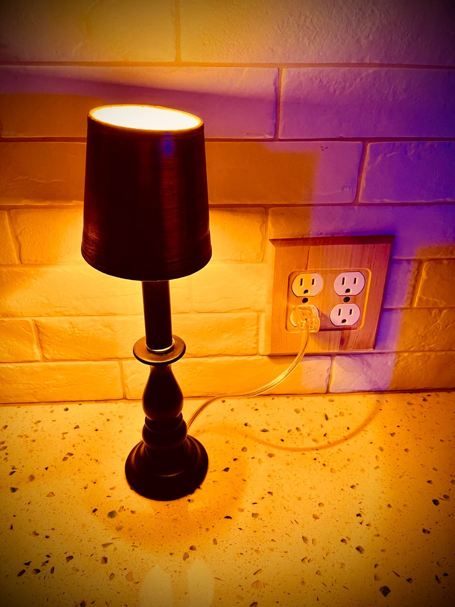 Black lamp plugged into a wooden outlet on a yellow-tiled surface.