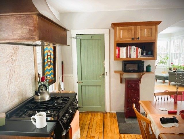 Kitchen with a gas stove, copper range hood, green door, wooden cabinets, and dining table.