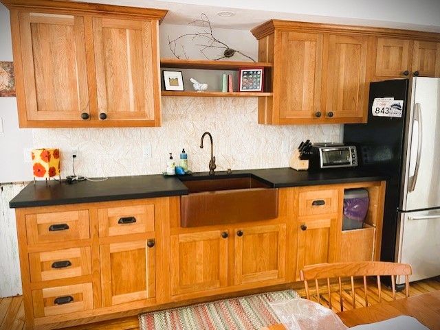 Wooden kitchen cabinets with dark countertops, copper sink, and a refrigerator.