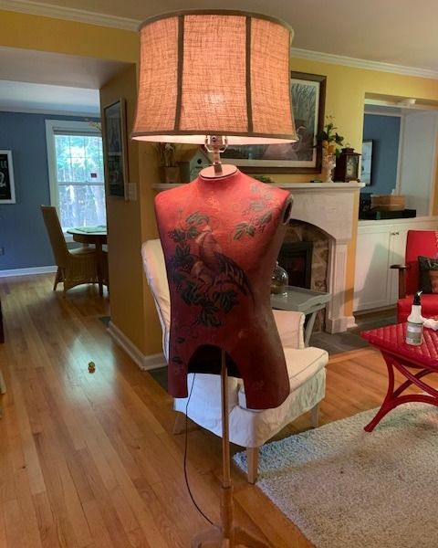 Mannequin lamp with a red torso, brown shade, and wooden stand in a living room.