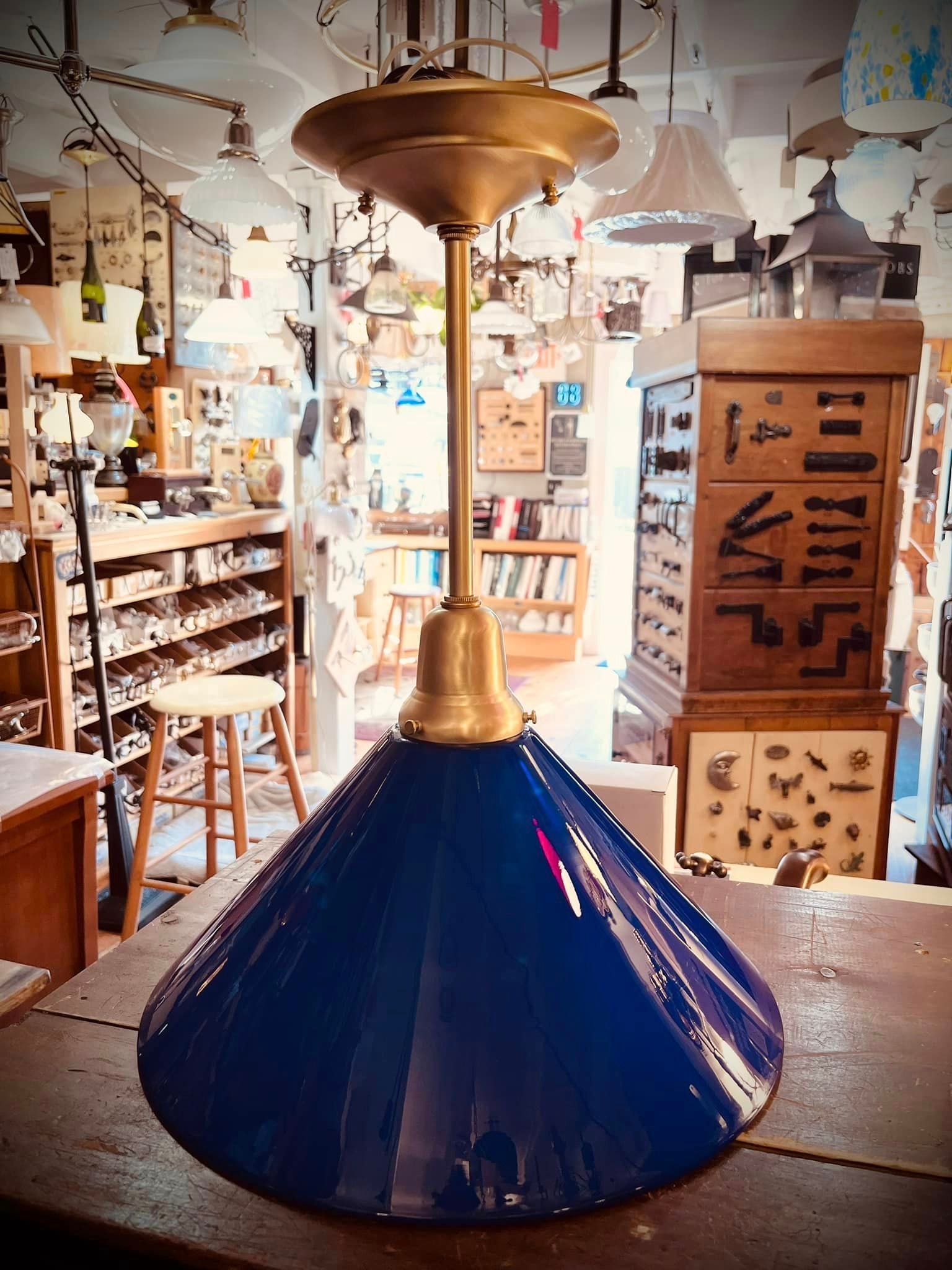 Blue glass pendant lamp in a shop, with brass fittings and other lamps in the background.