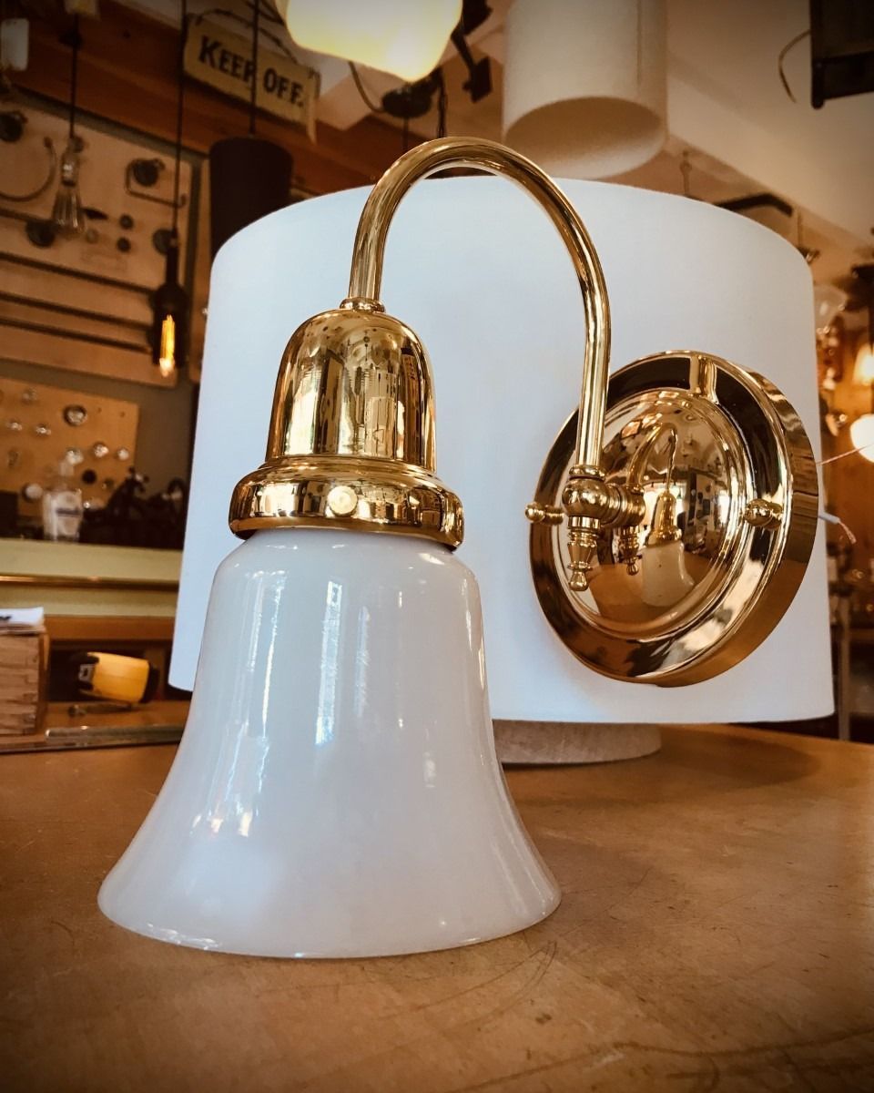 White glass lamp with gold fixture, mounted on a wall with a cylindrical lampshade.
