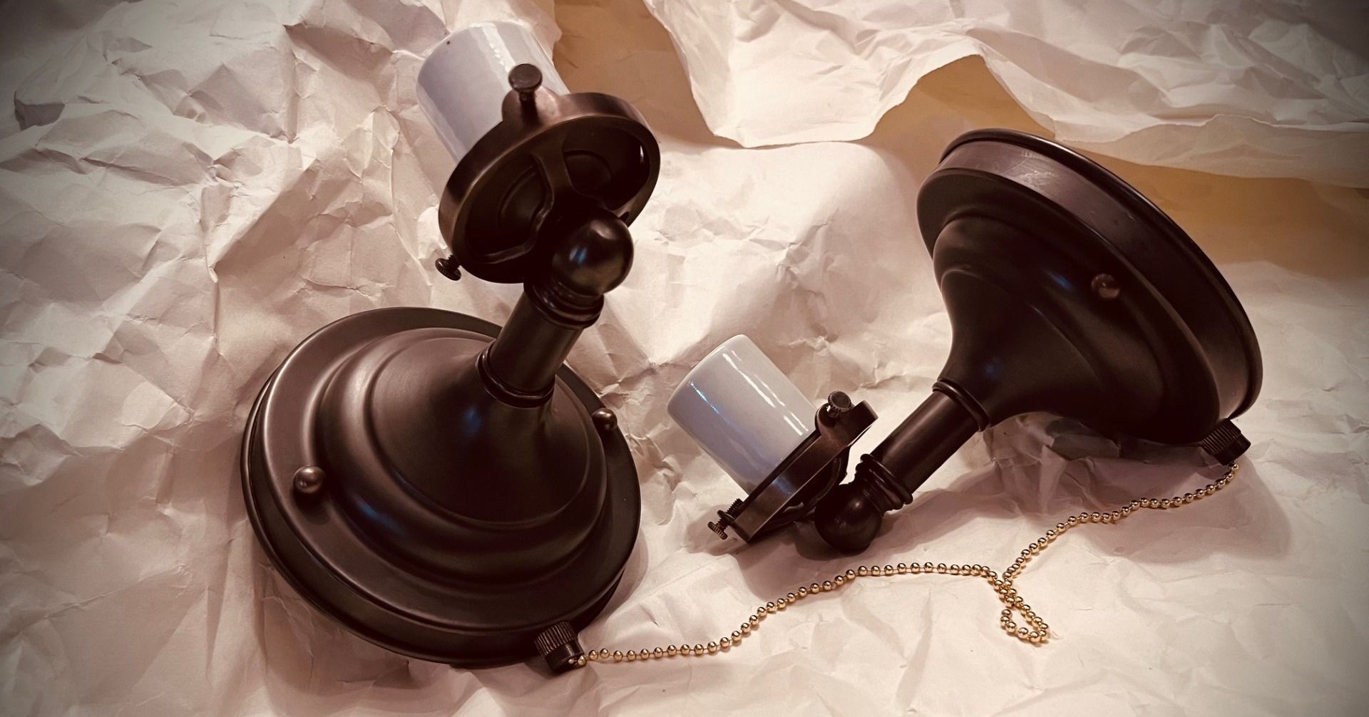 Two antique bronze-colored light fixtures with pull chains, set on crumpled paper.
