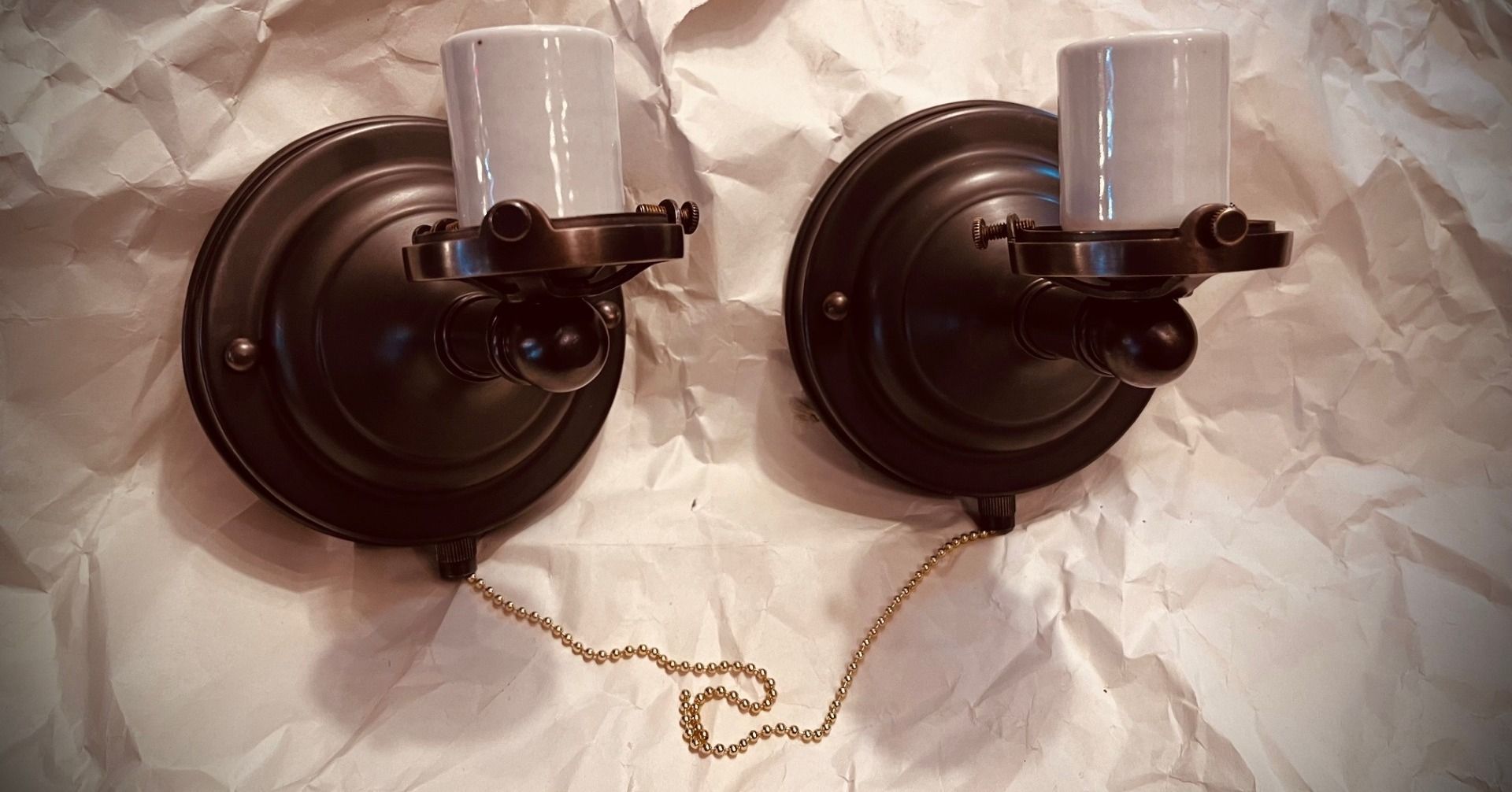 Two dark bronze wall sconces with white bulb sockets, pull chains.