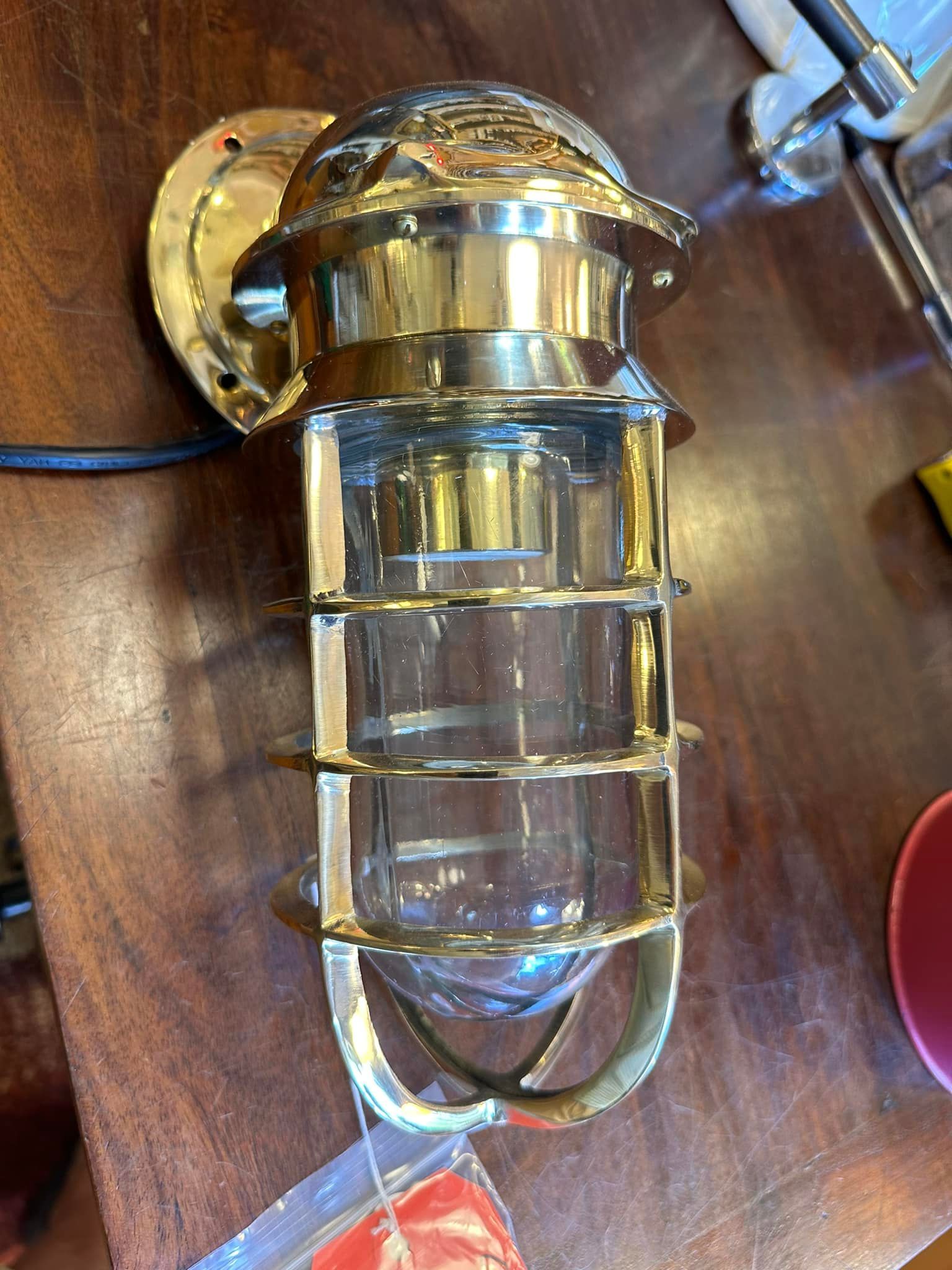 Brass nautical-style wall light fixture with a wire and clear glass lens cage.
