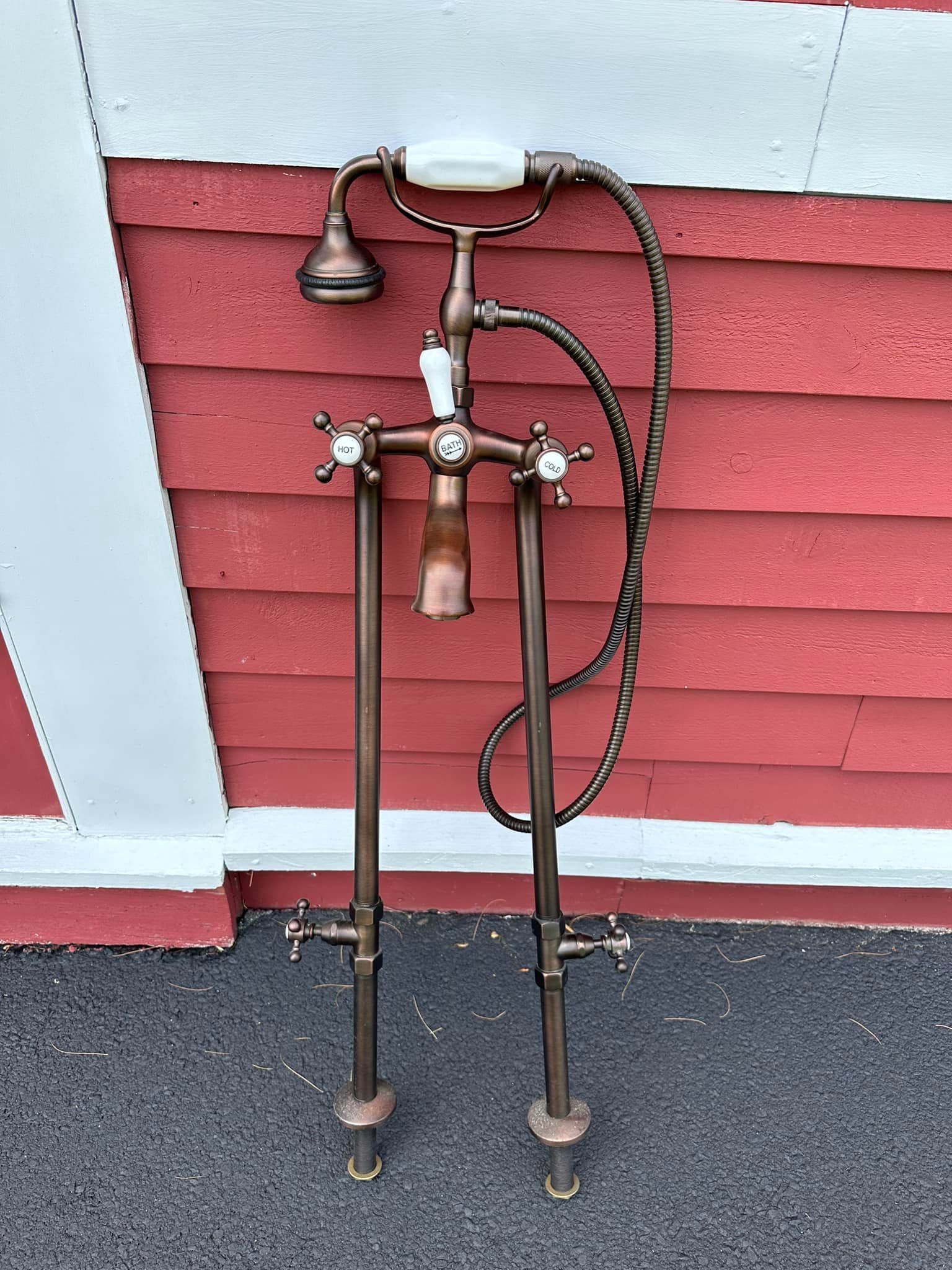 Bronze freestanding bathtub faucet with showerhead against a red wall.