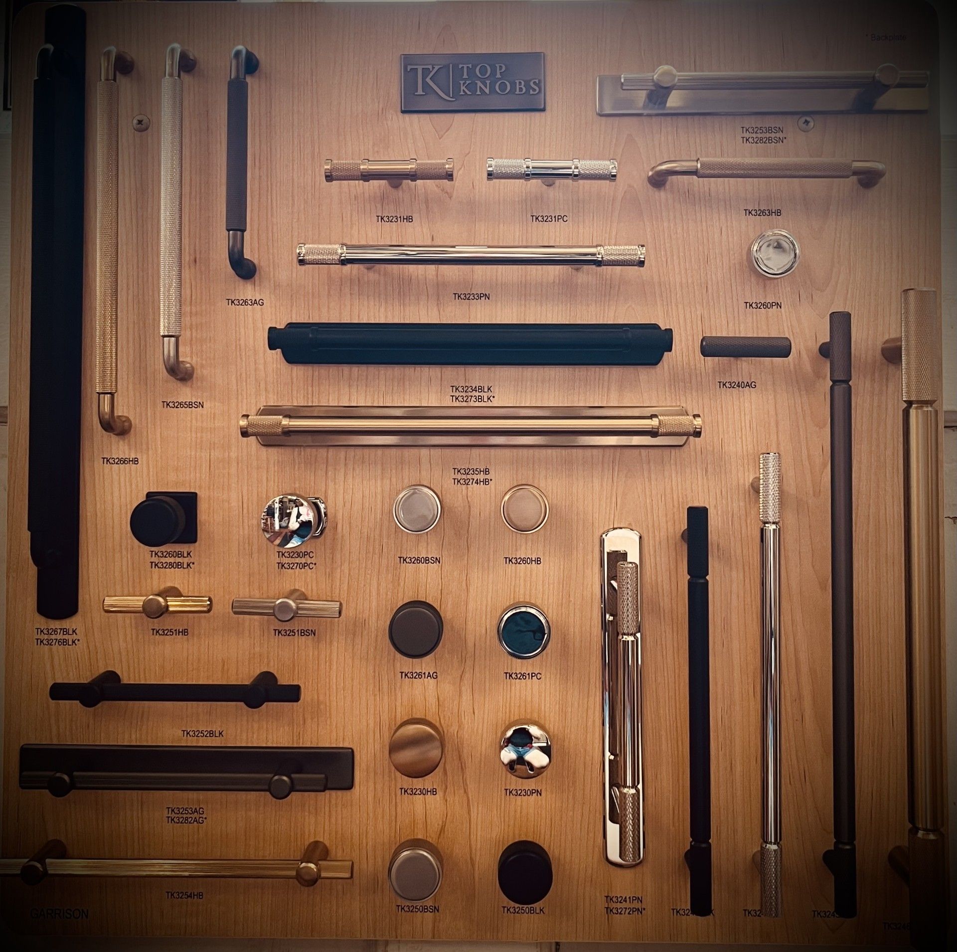 Display board of various door hardware samples, including pulls, knobs, and latches, in brass, black, and silver.