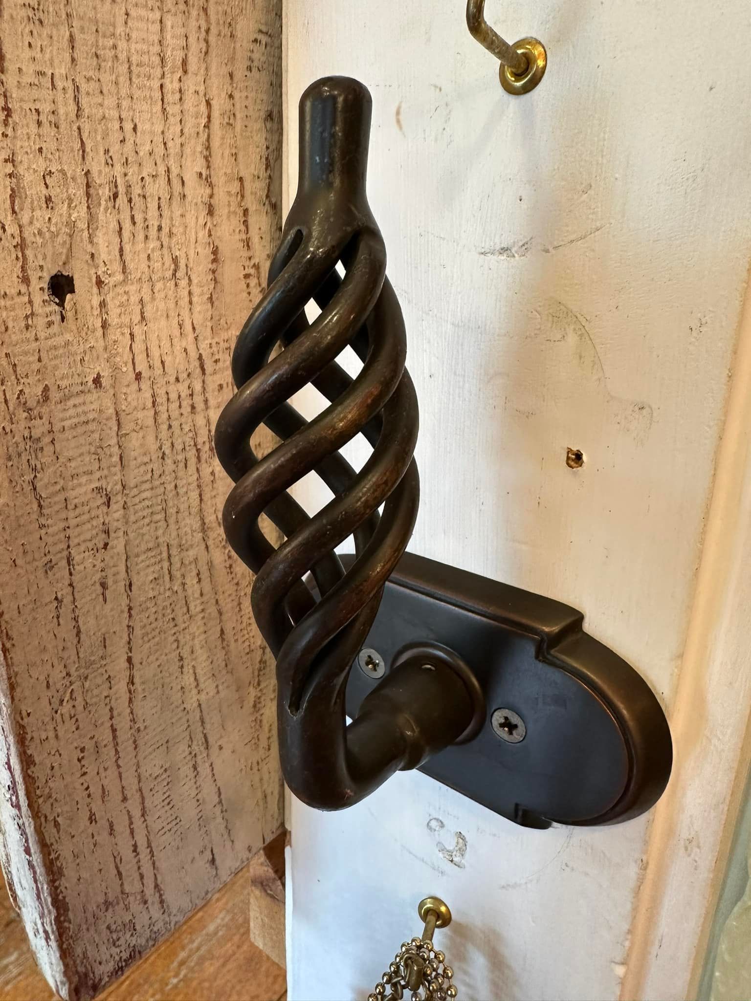 Dark bronze, ornate door handle with twisted cage design on white door.