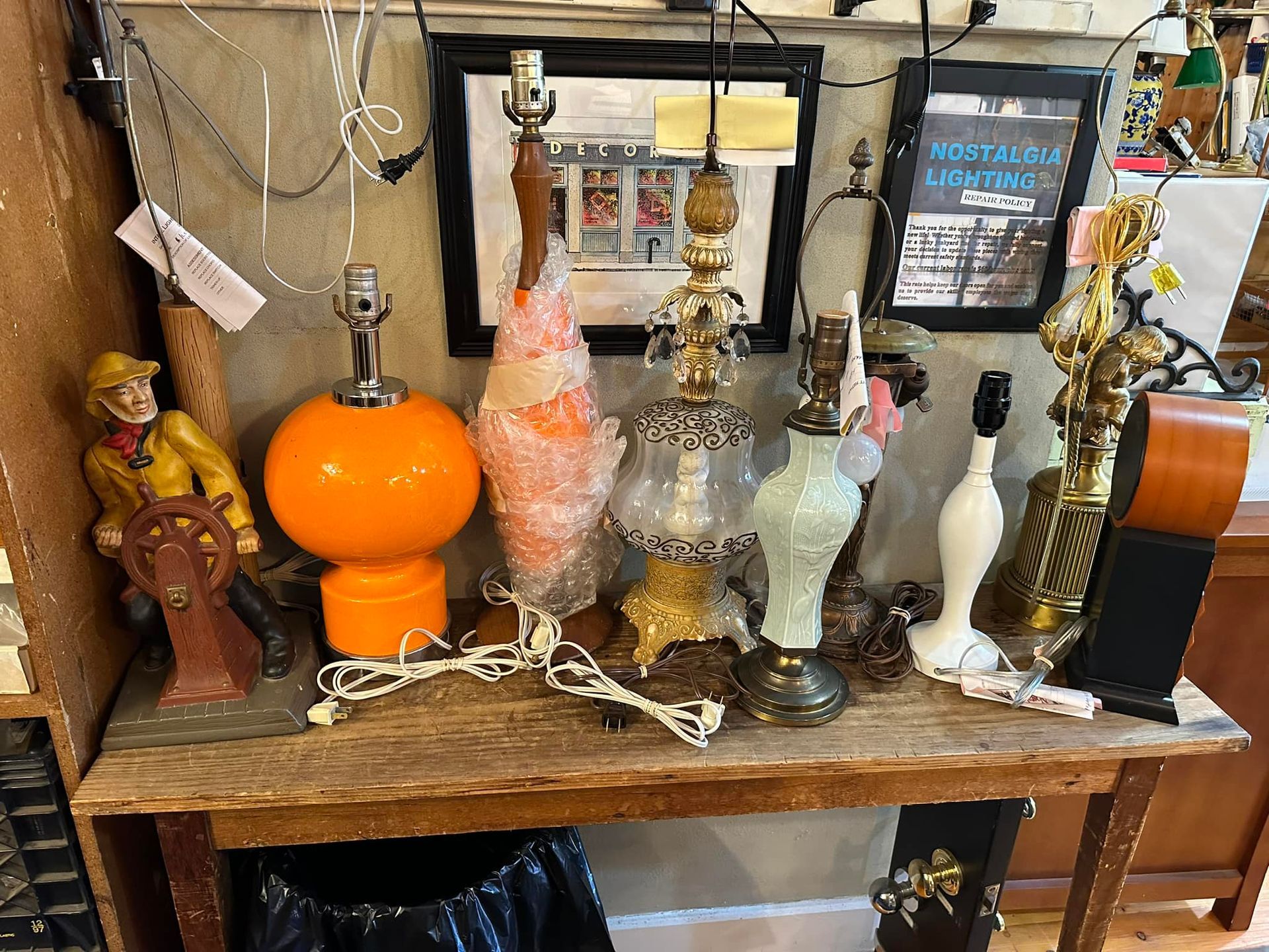 Several antique lamps on a wooden table, including orange, glass, and brass styles.