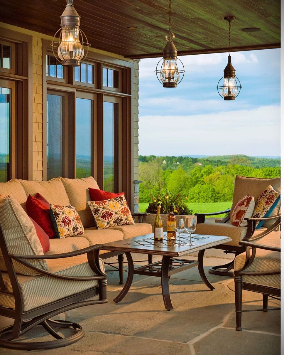 Covered patio with outdoor furniture, overlooking a green landscape and blue sky.