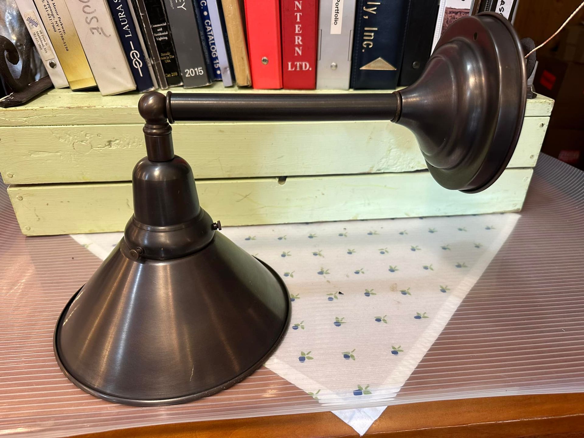 Metal wall sconce with conical shade, mounted on a wall; books in the background.