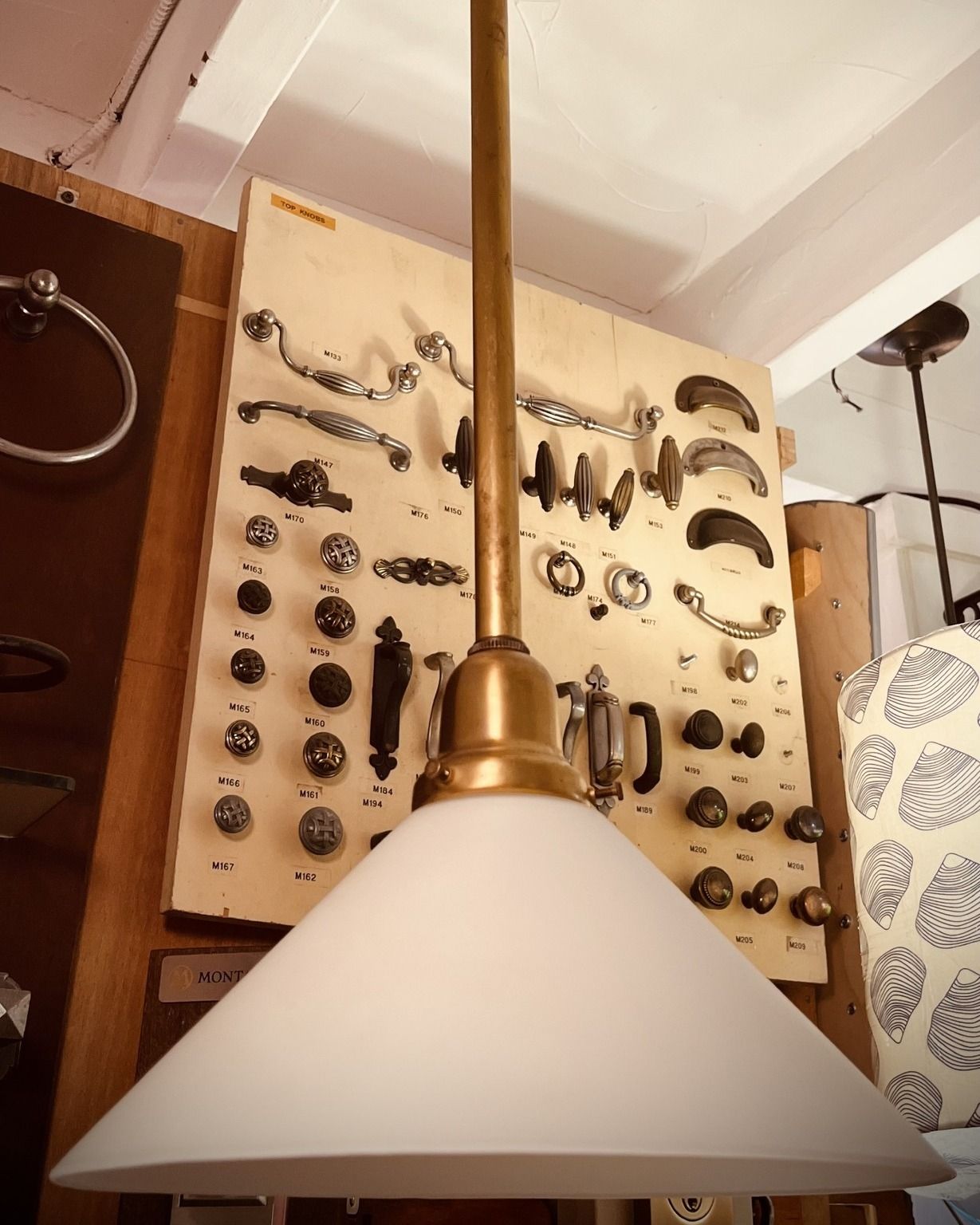 Brass pendant light with a white cone shade, hardware display background.