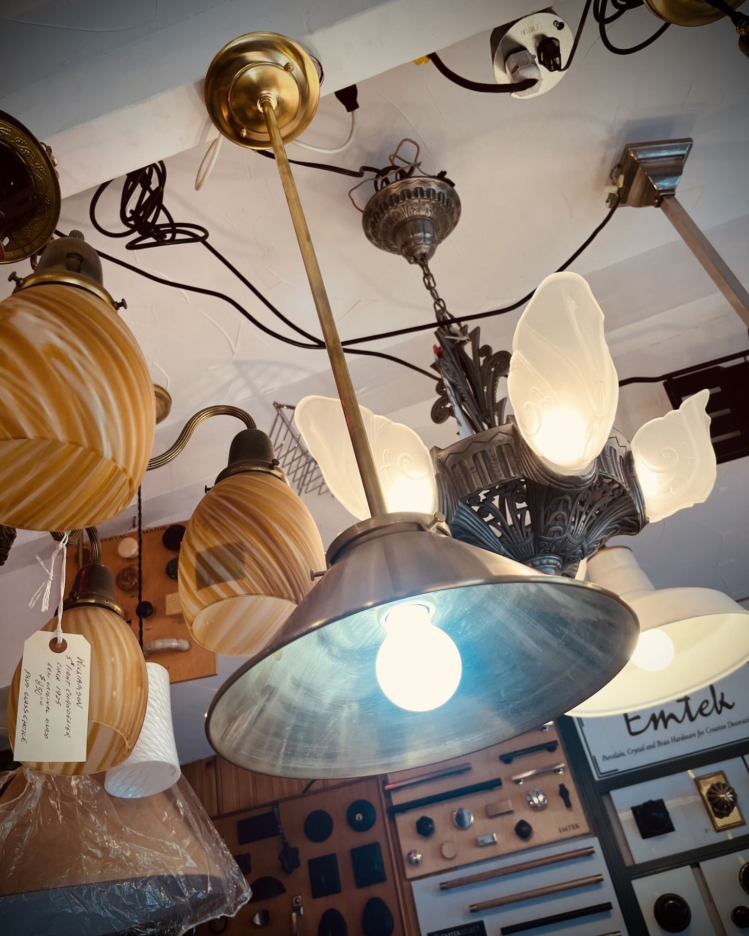 Antique light fixtures hanging in a shop, showcasing diverse designs, including a pendant lamp with a lit bulb.