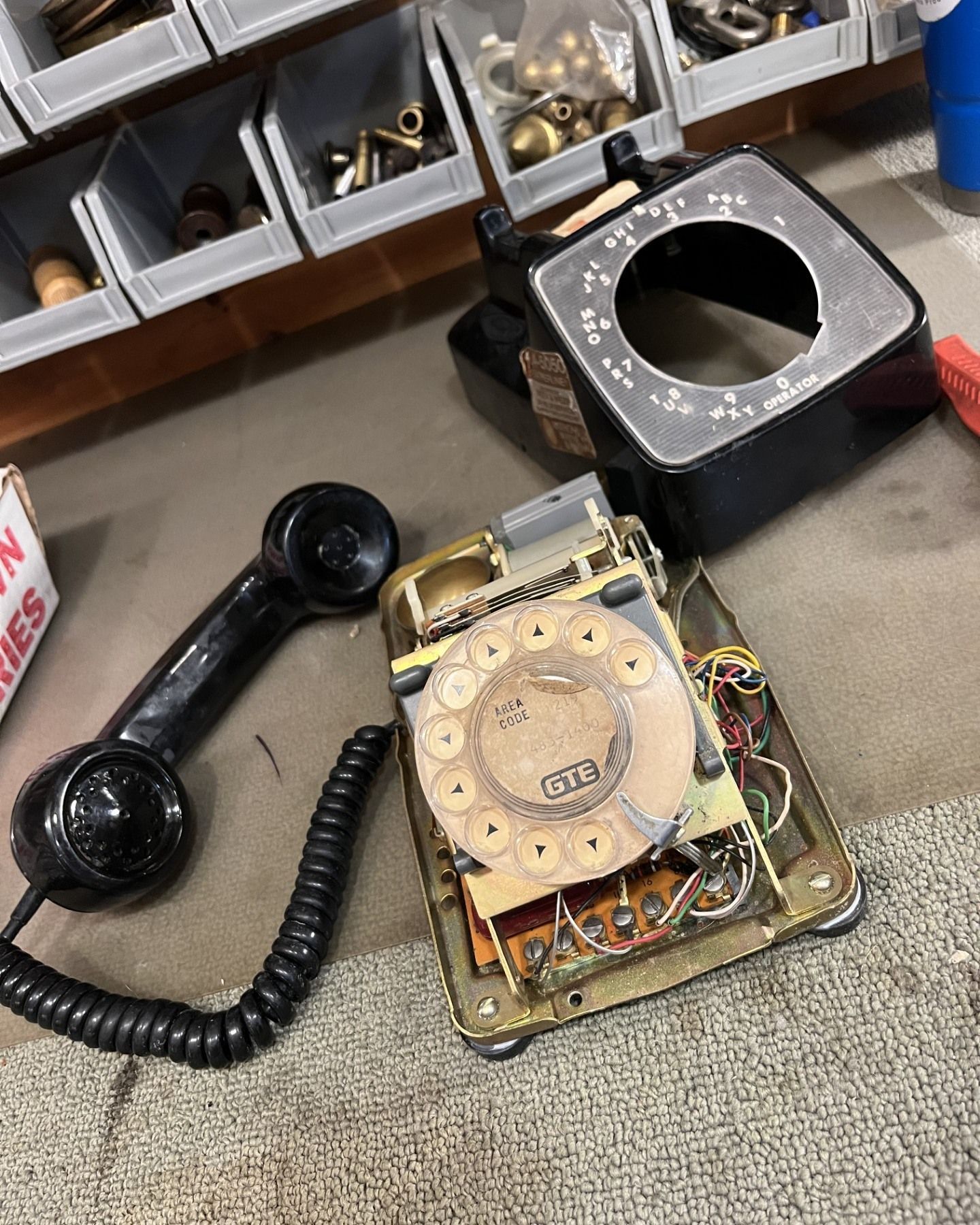 Black rotary telephone, disassembled on a workbench. Handset, dial, and internal components visible.