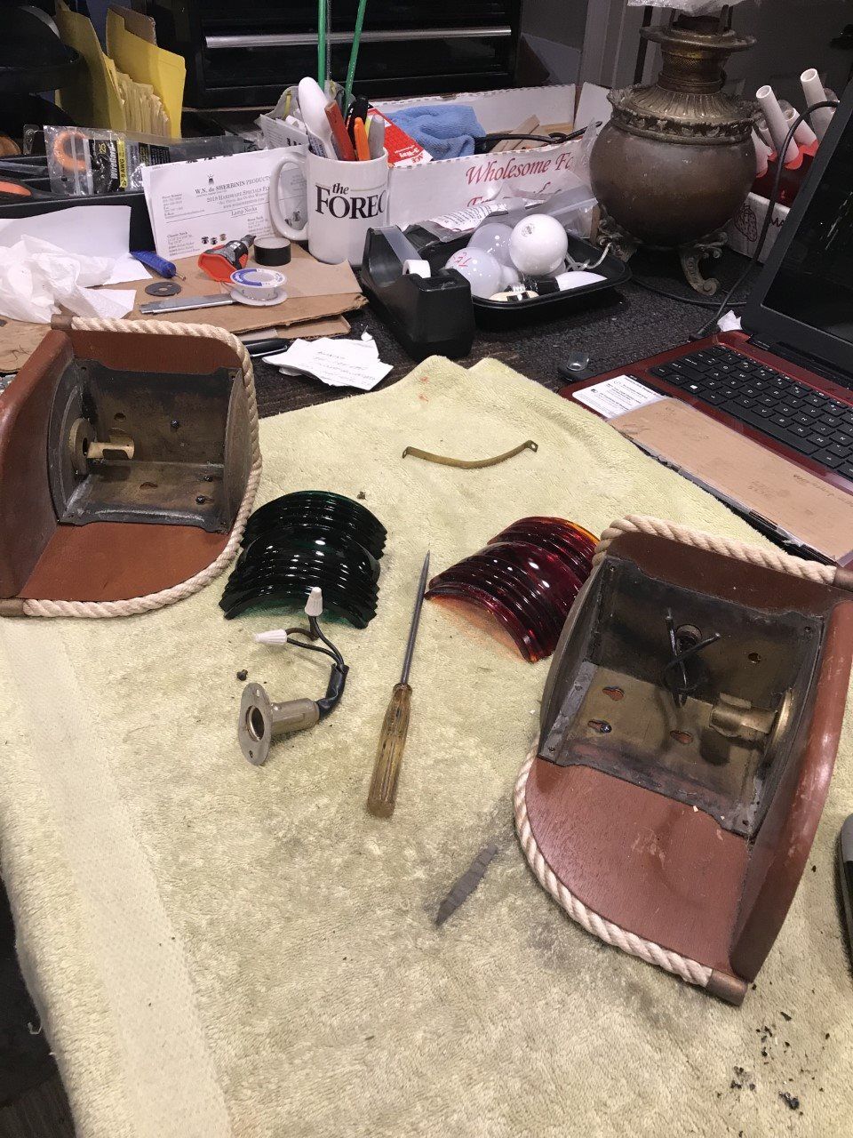 Two vintage car taillight housings with broken lenses and tools on a towel-covered workbench.