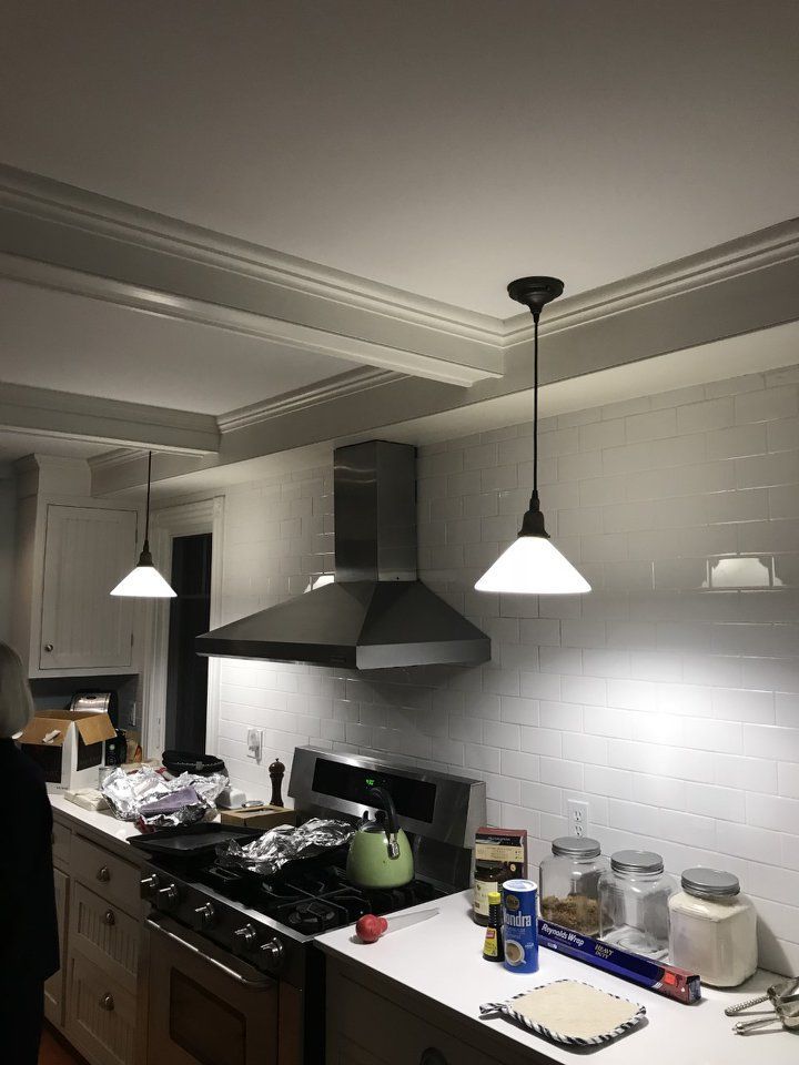 Kitchen with white tile backsplash, stainless steel hood, hanging pendant lights, and overhead beams.