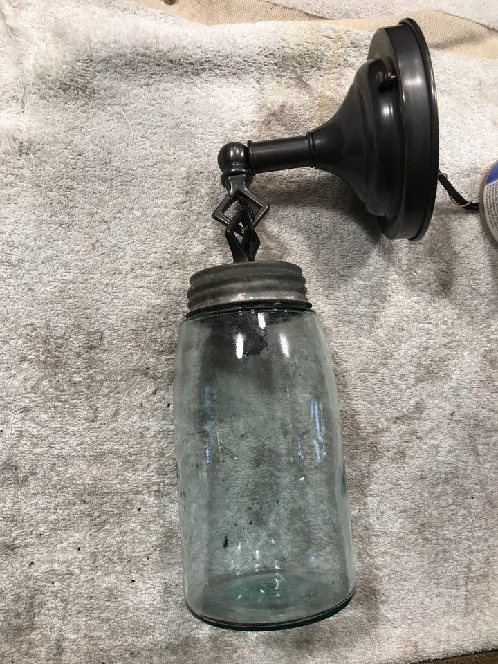 Dark metal wall-mounted light fixture with a blue mason jar as a lampshade, on a light-colored surface.