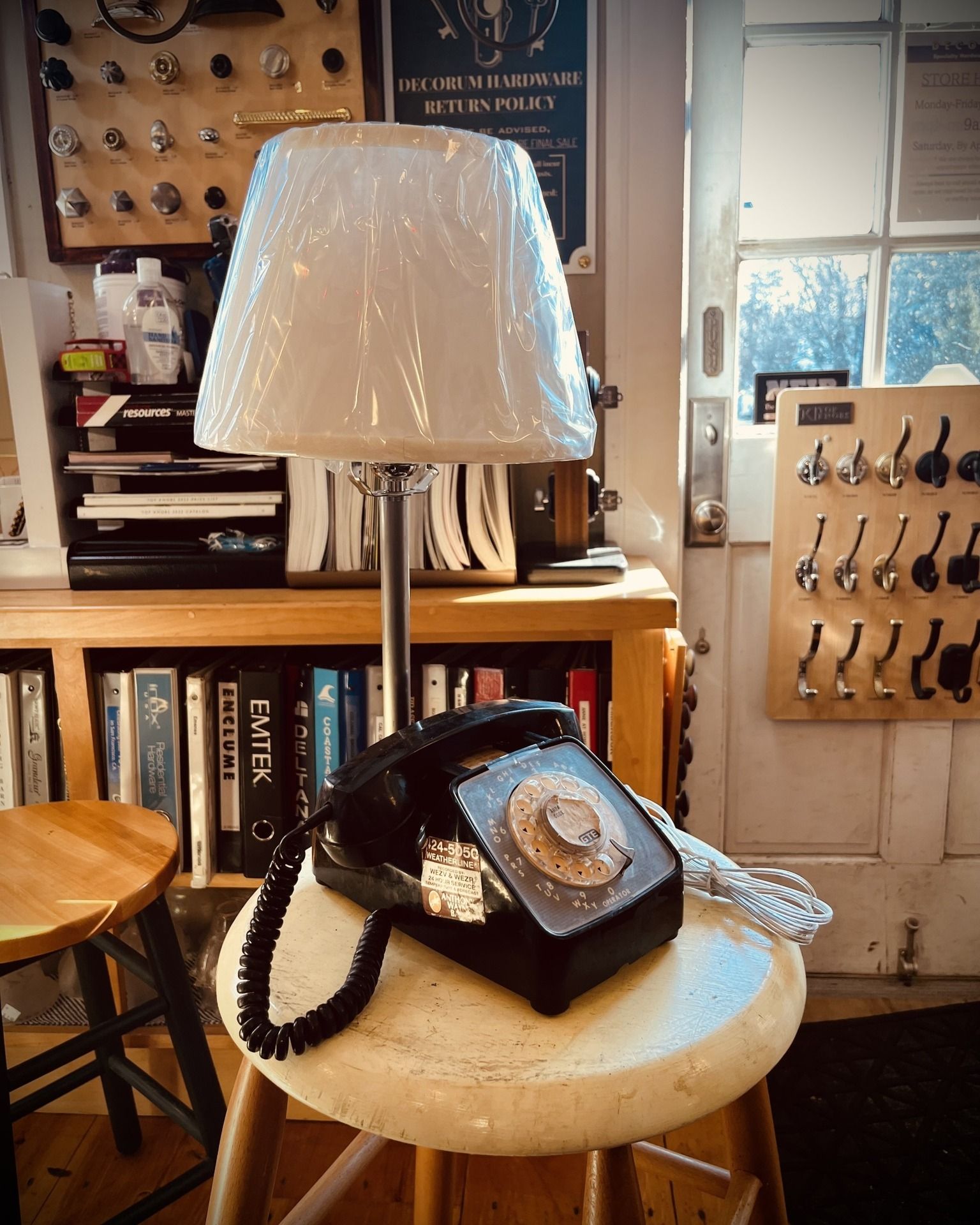 Black rotary phone and lamp on a stool in a room with books and coat hooks.