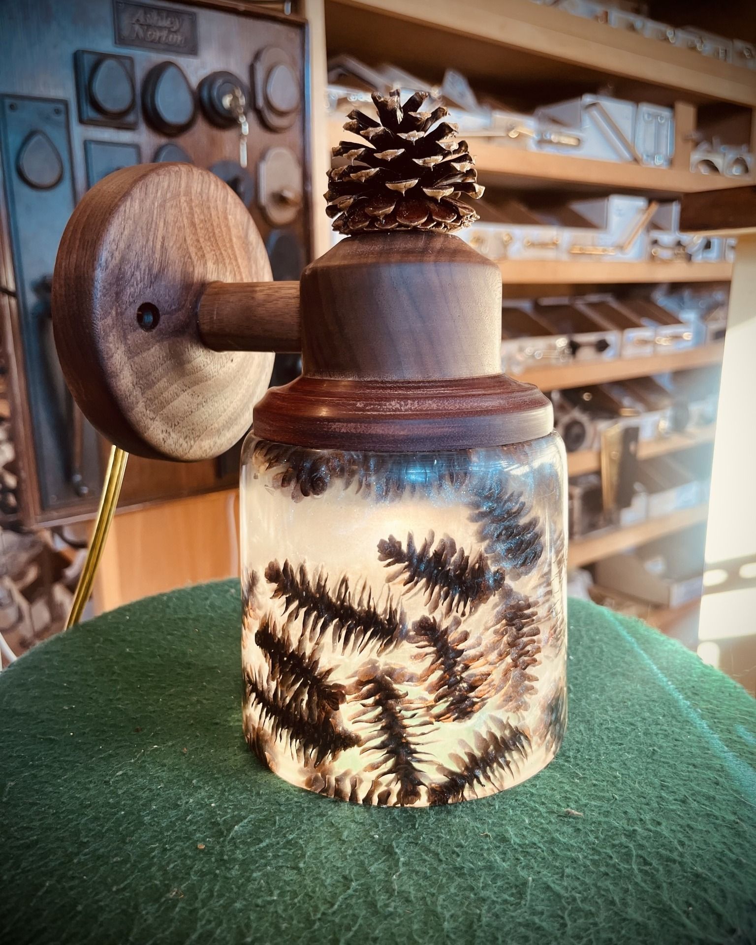 Wooden wall lamp with a pine cone detail, encased evergreen branches.