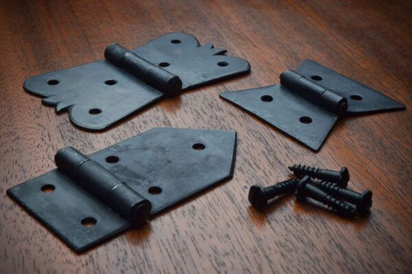 Black decorative hinges and screws on a wooden surface.
