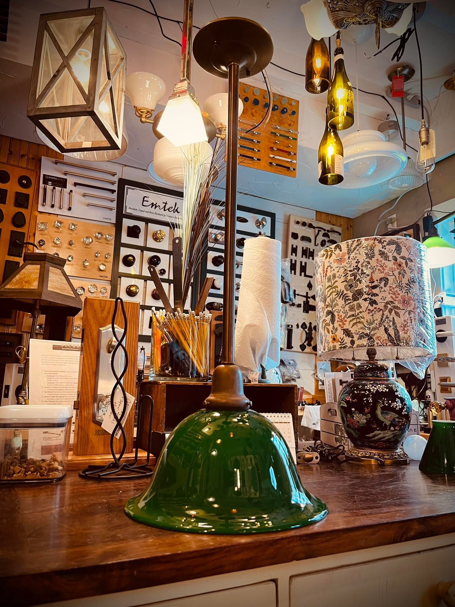 Green glass pendant lamp on display in a store, with other lamps and fixtures in the background.