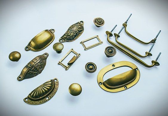 Various antique-style brass cabinet pulls and knobs, scattered on a white surface.
