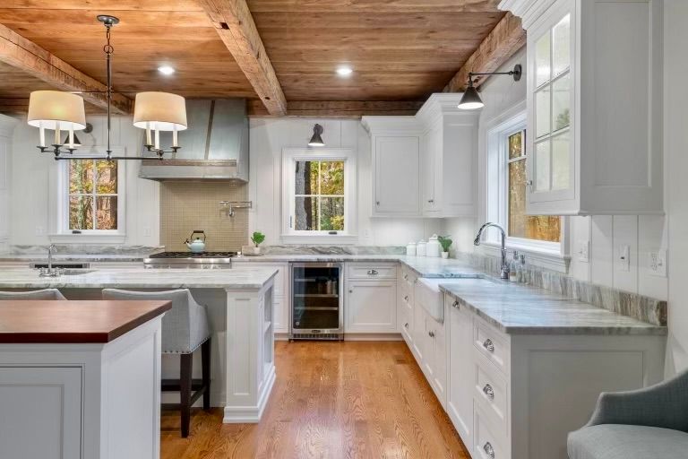 White kitchen with wooden ceiling, island, and countertops; windows with a view.