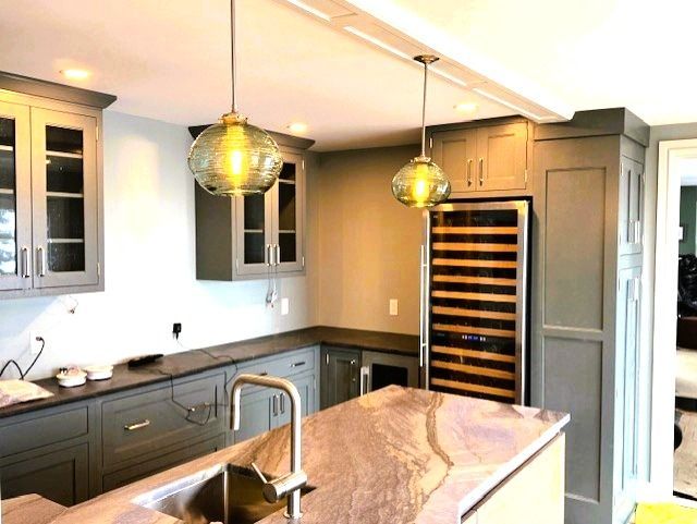 Kitchen with gray cabinets, a granite countertop, and two pendant lights. A wine cooler is built-in.
