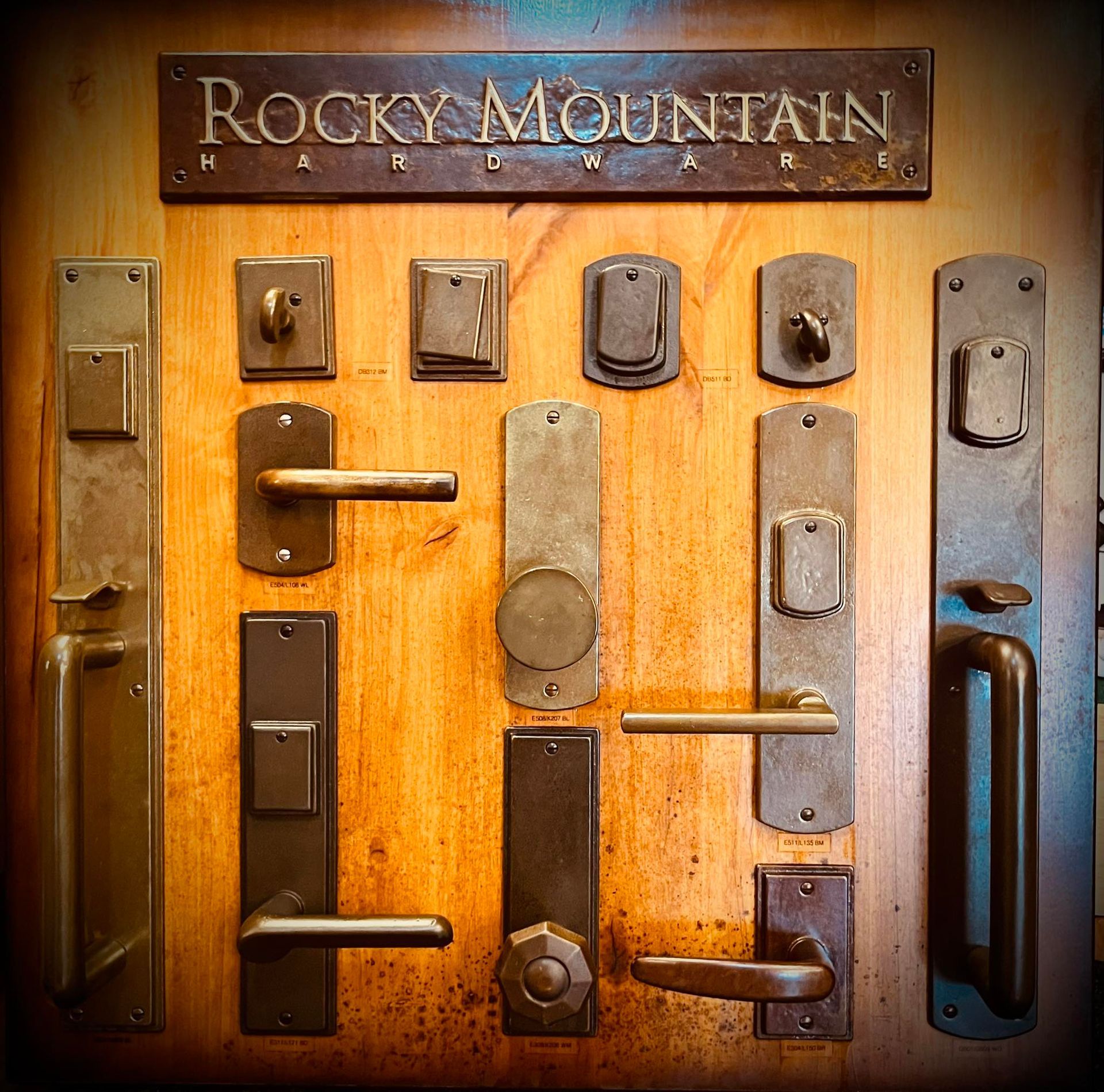 Display of bronze Rocky Mountain Hardware door handles and locks on wooden board.