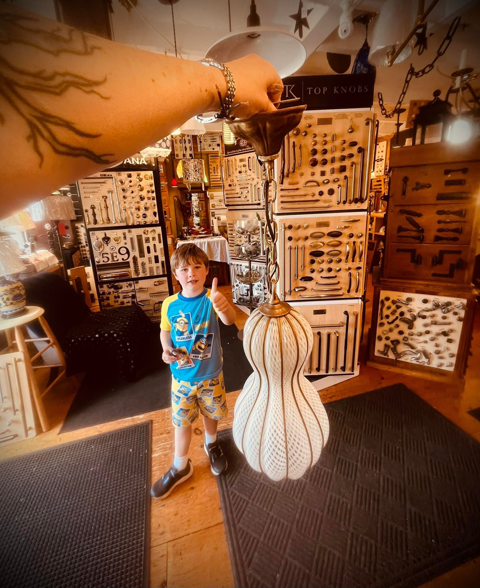 Person holds a vintage light fixture; child stands nearby. Interior with many displayed items.