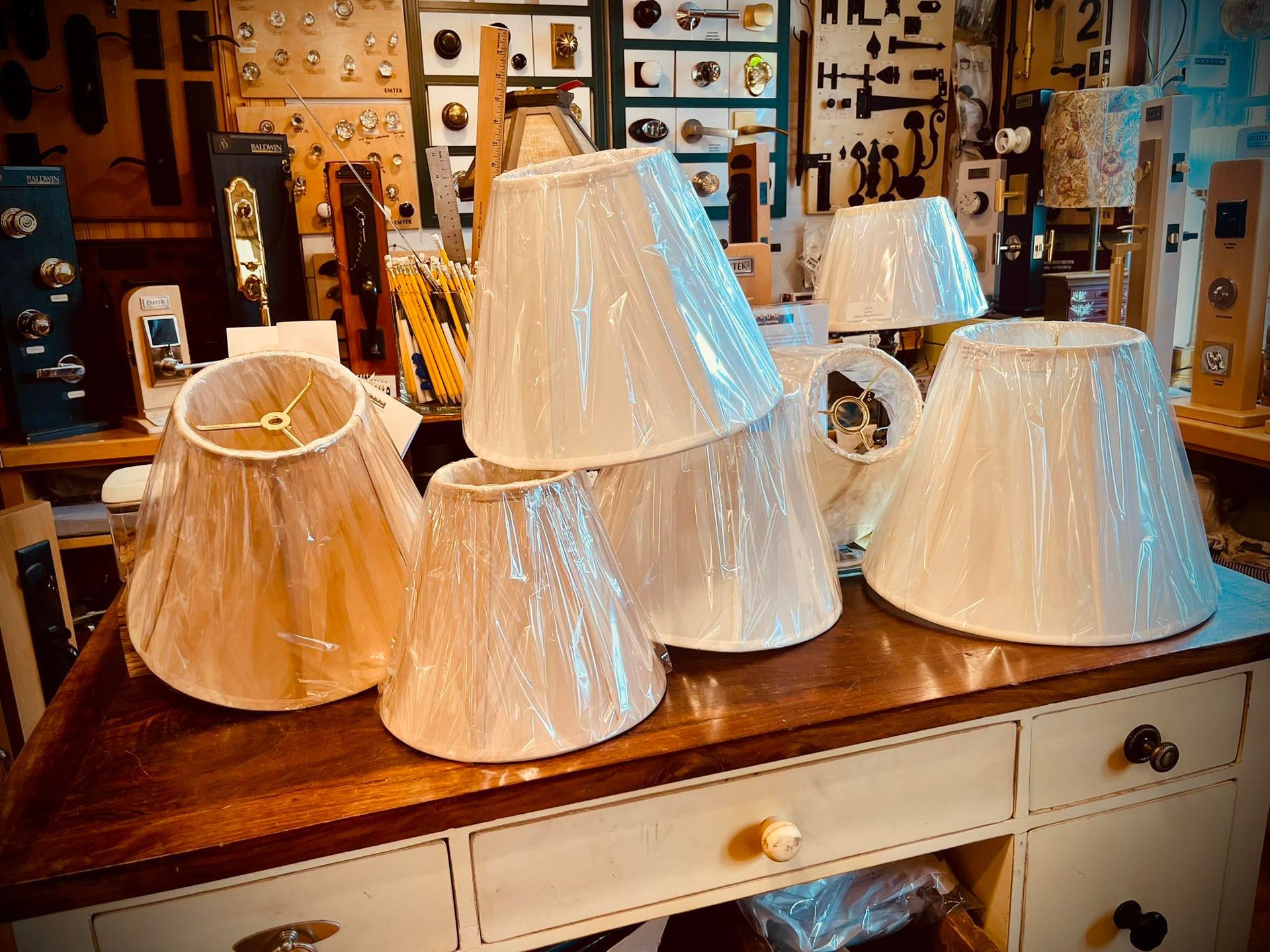Stack of ivory lamp shades on a wooden desk, hardware store background.