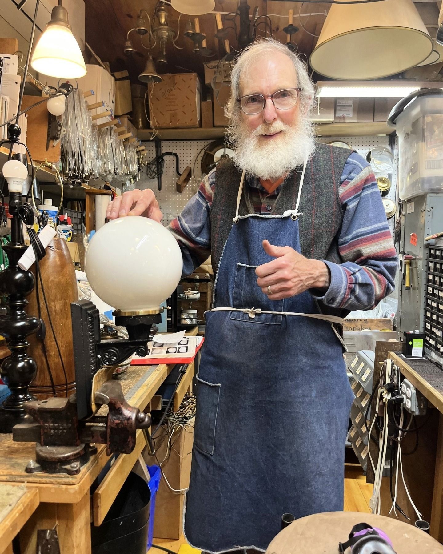 Man in apron holding a white globe lamp, in a workshop with lights and tools.