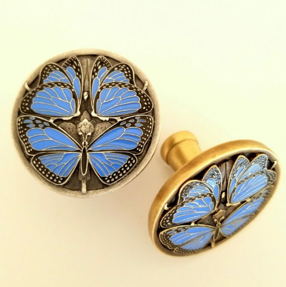 Two decorative butterfly cabinet knobs, blue and silver, on a white surface.