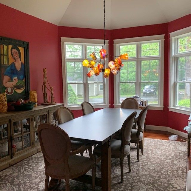 Dining room with red walls, white trim, and a colorful chandelier above a dark table surrounded by chairs.