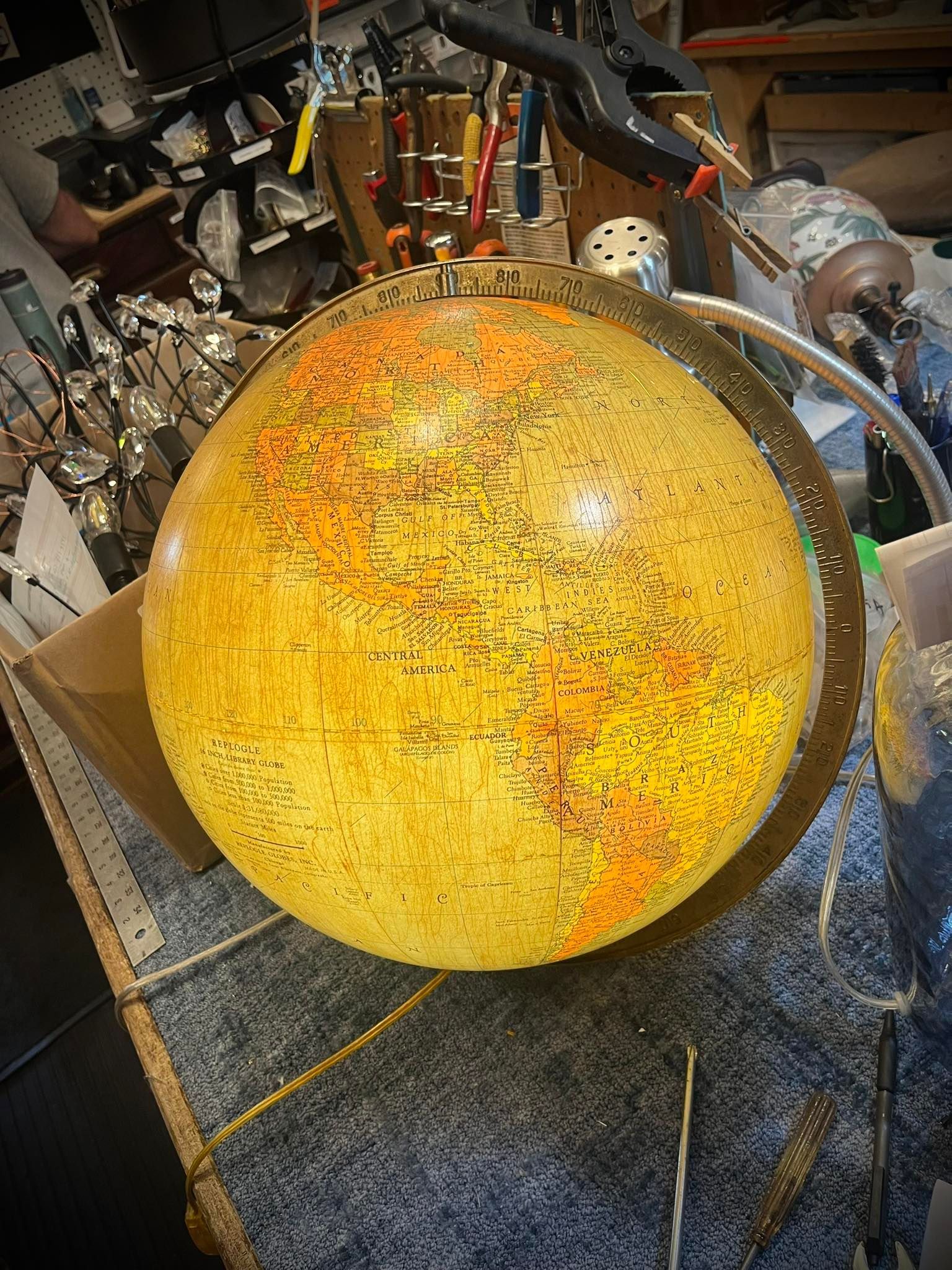 Glowing globe, orange and yellow, in a workshop setting with tools and cluttered surface.