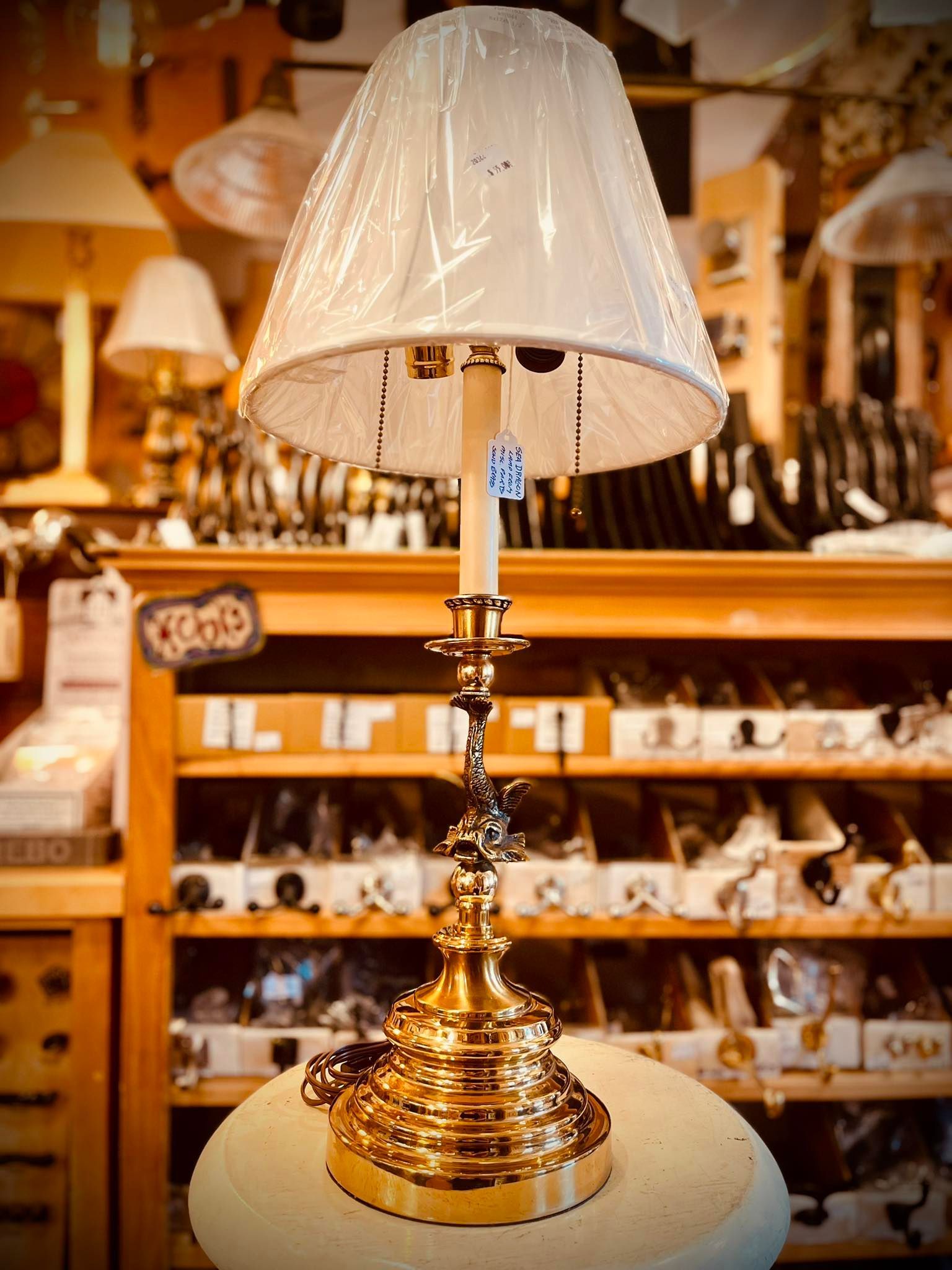 Brass candlestick lamp with a white lampshade on display in a store.