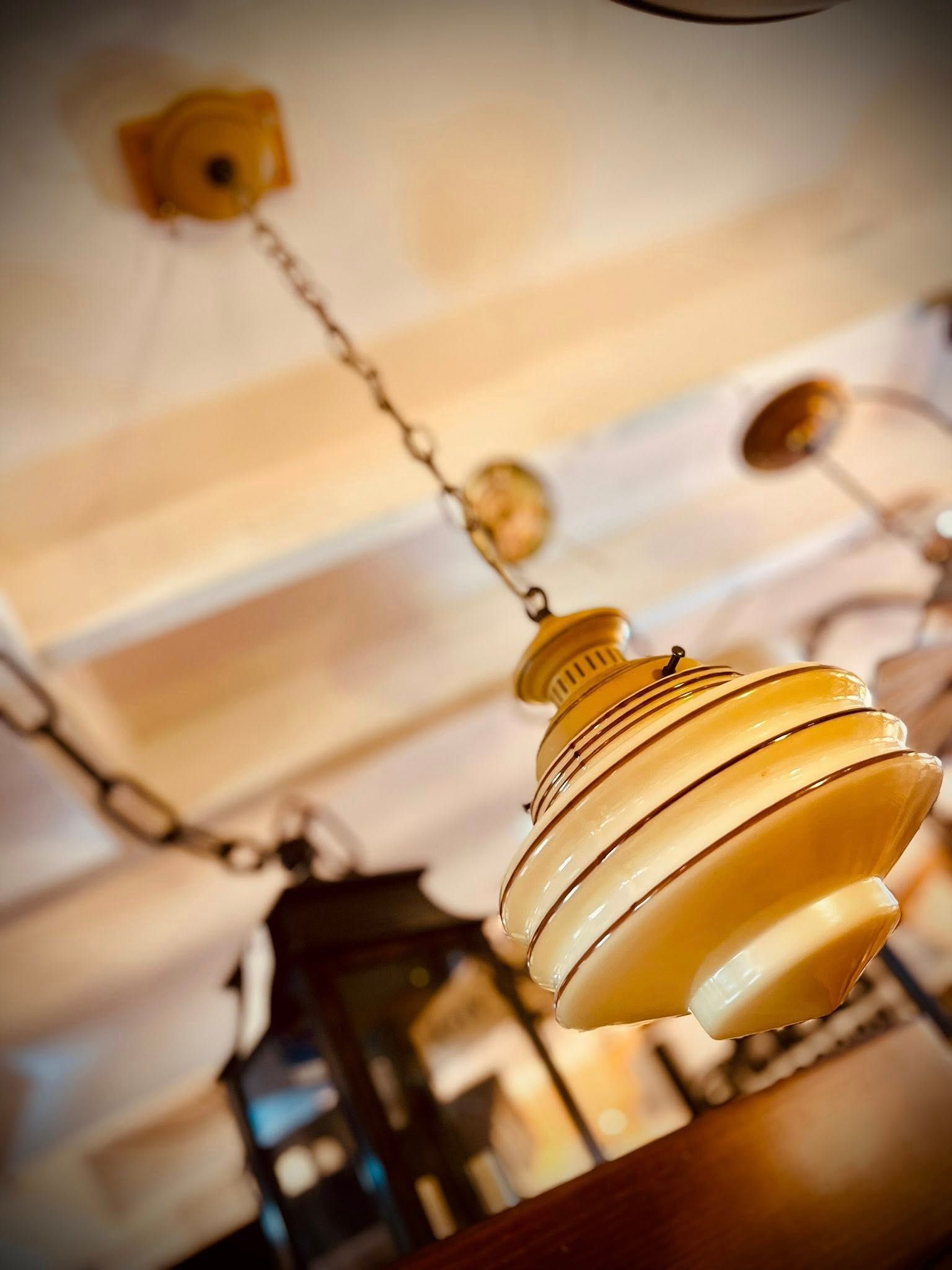 Antique pendant light with a cream-colored, tiered glass shade hanging from a chain.