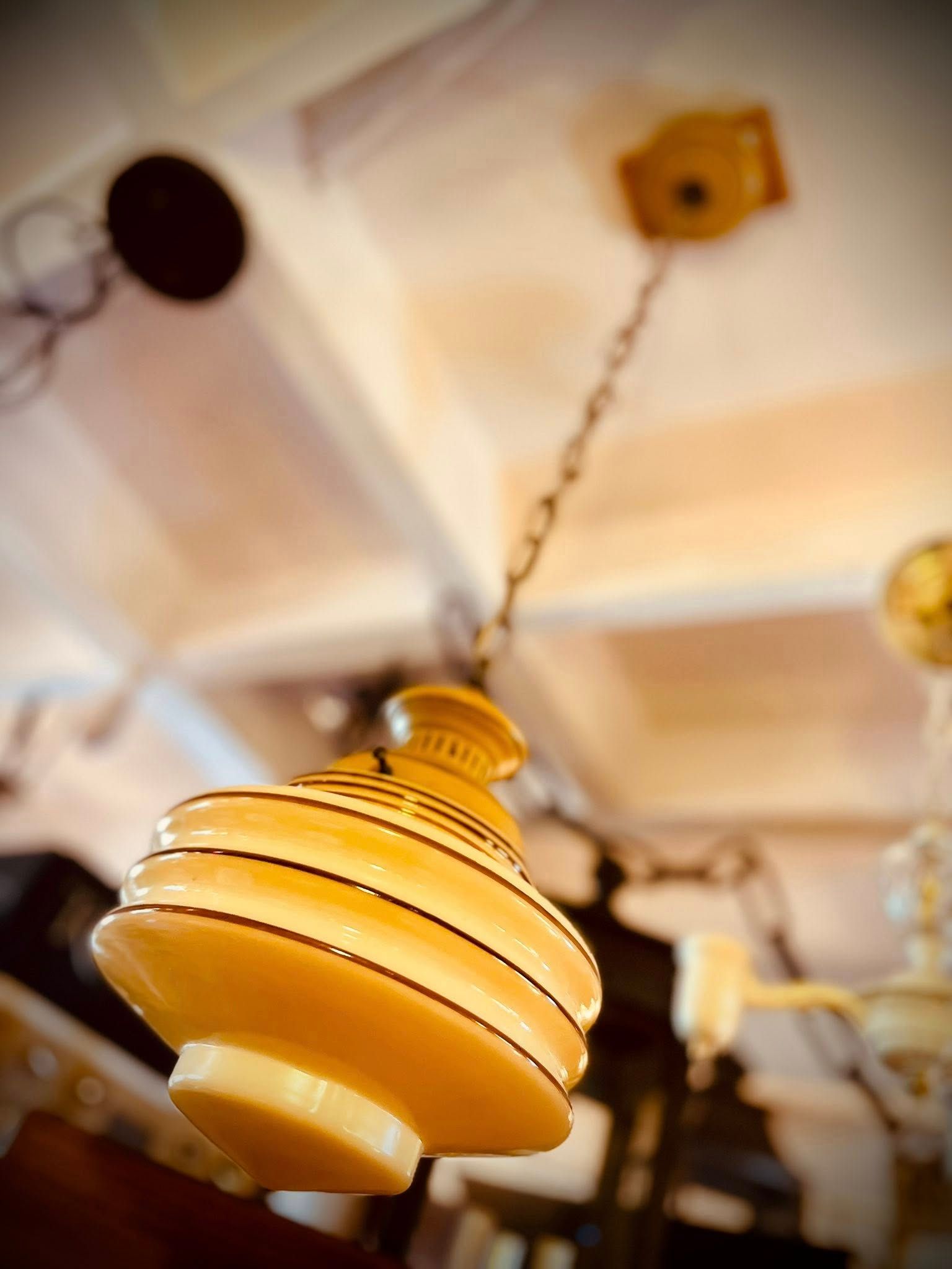 Yellow, art deco style hanging light fixture suspended from a chain on a white ceiling.