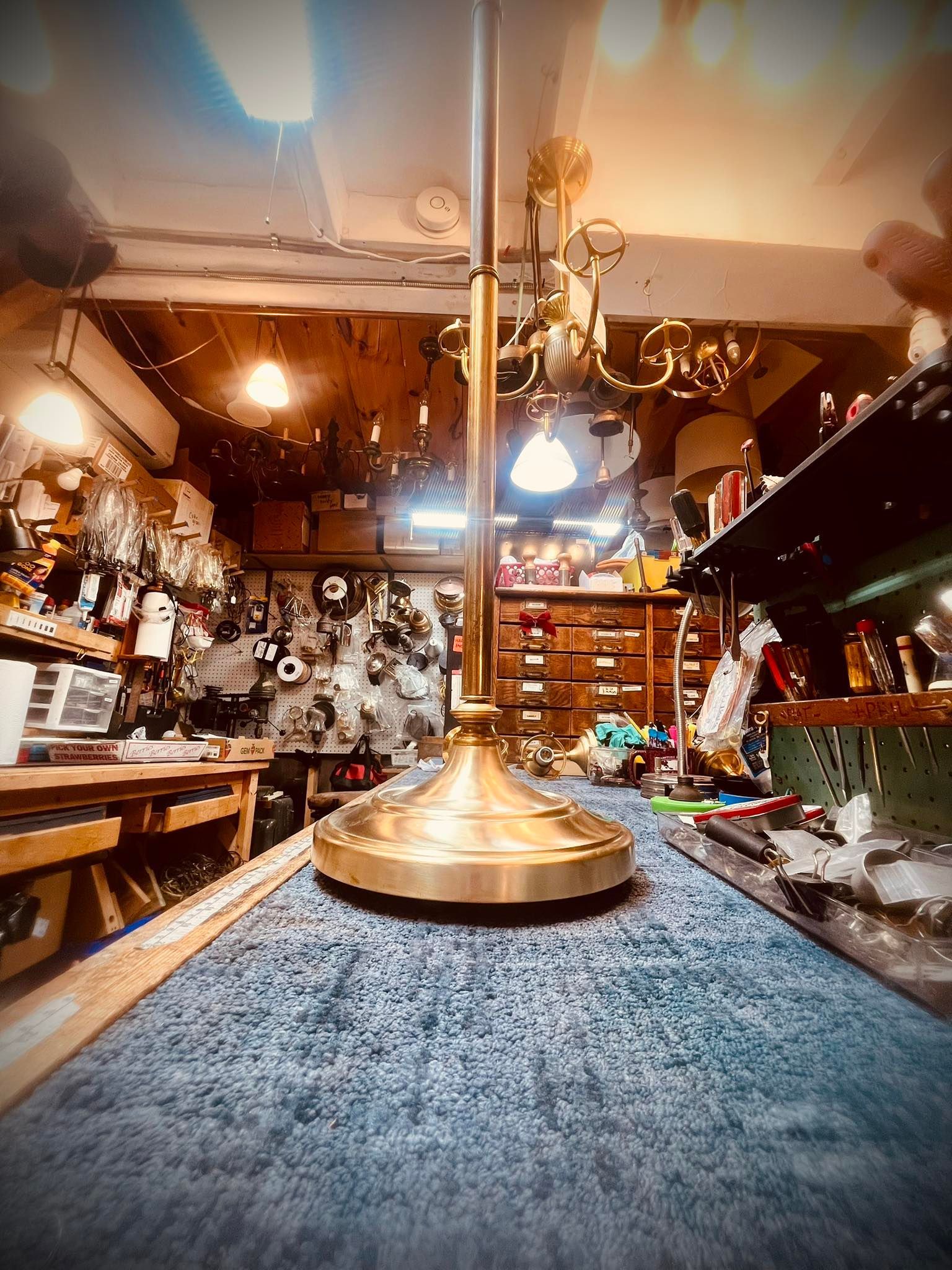 Brass lamp base on a table in a cluttered workshop, with tools and parts visible in the background.