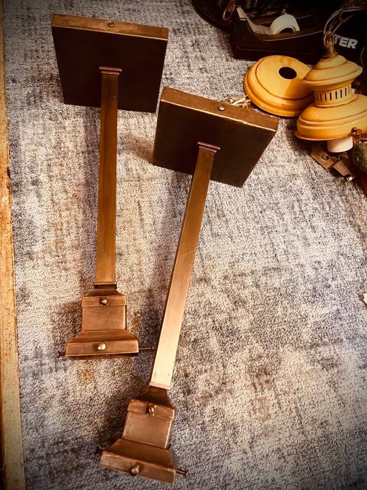 Two bronze-toned display stands with square tops, angled on a textured surface.