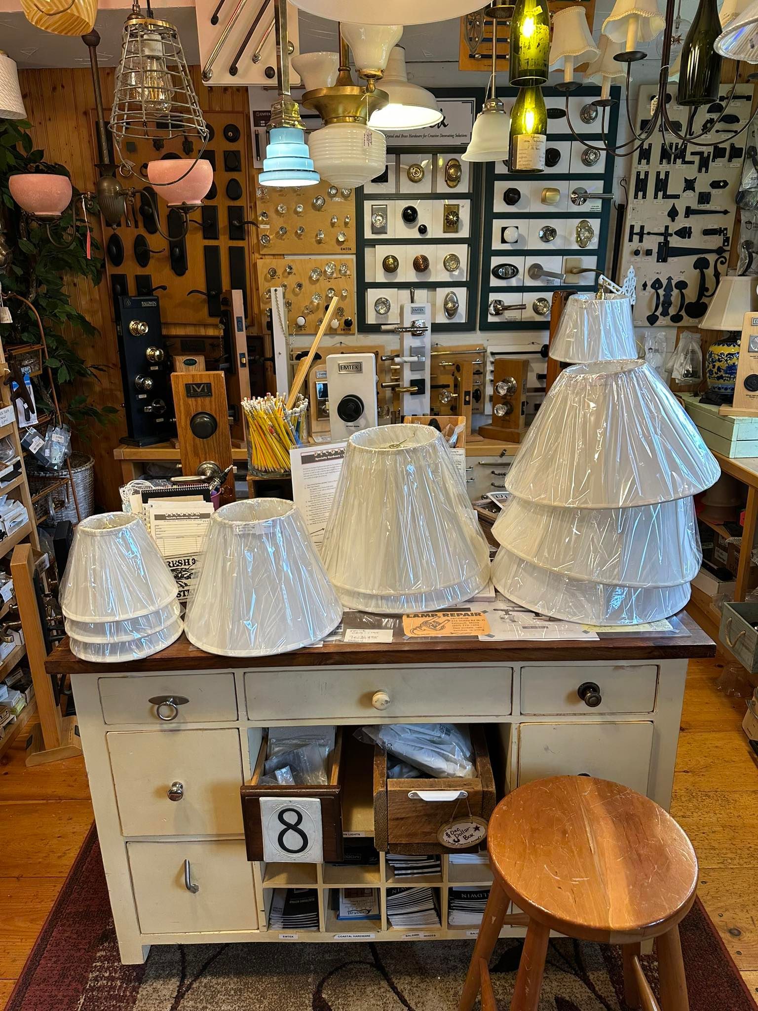 White lampshades on a vintage cabinet, many other light fixtures in a shop setting.