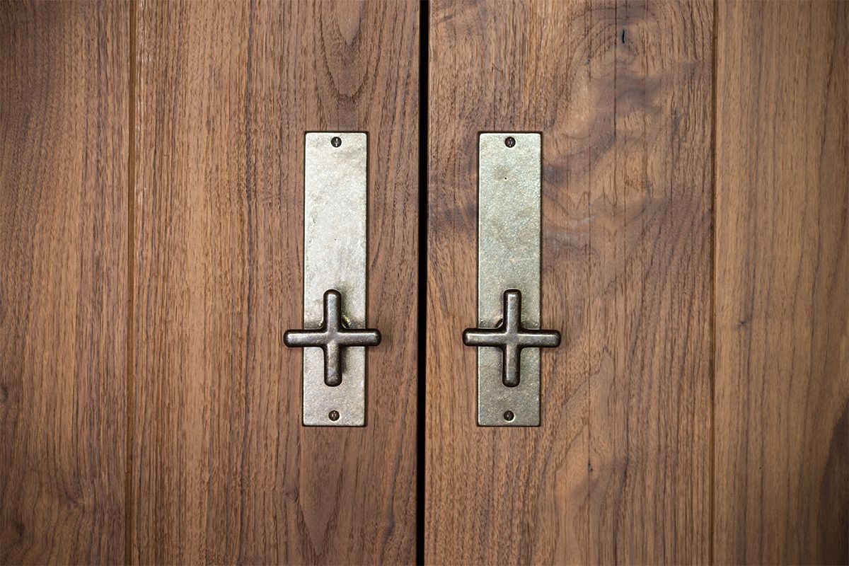 Close-up of two wooden cabinet doors with vertical rectangular metal handles and plus-sign style pulls.