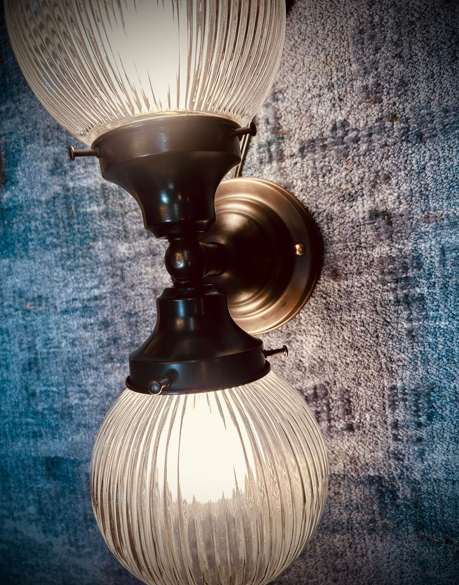 Double-globe wall sconce with textured glass, black and brass fixtures against a blue, textured wall.