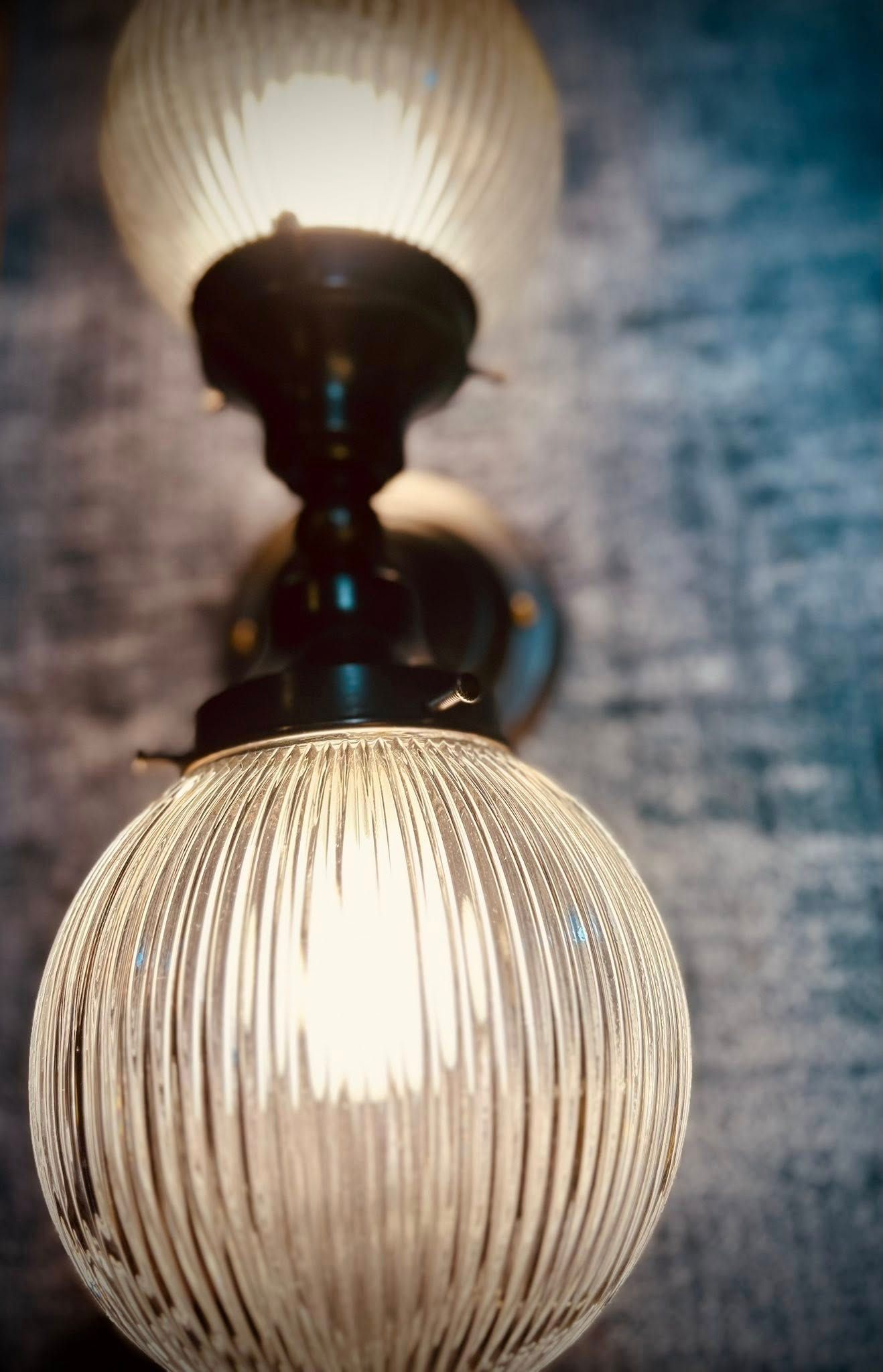 Two-bulb sconce with ribbed glass globes, lit against a textured wall.