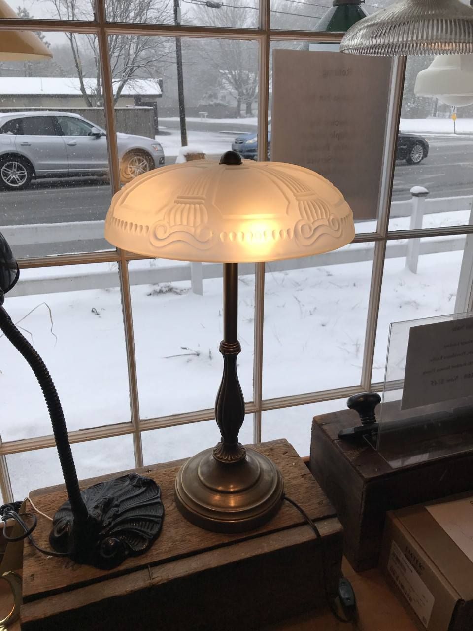 Antique brass table lamp with a frosted glass shade, snowy outdoor background.